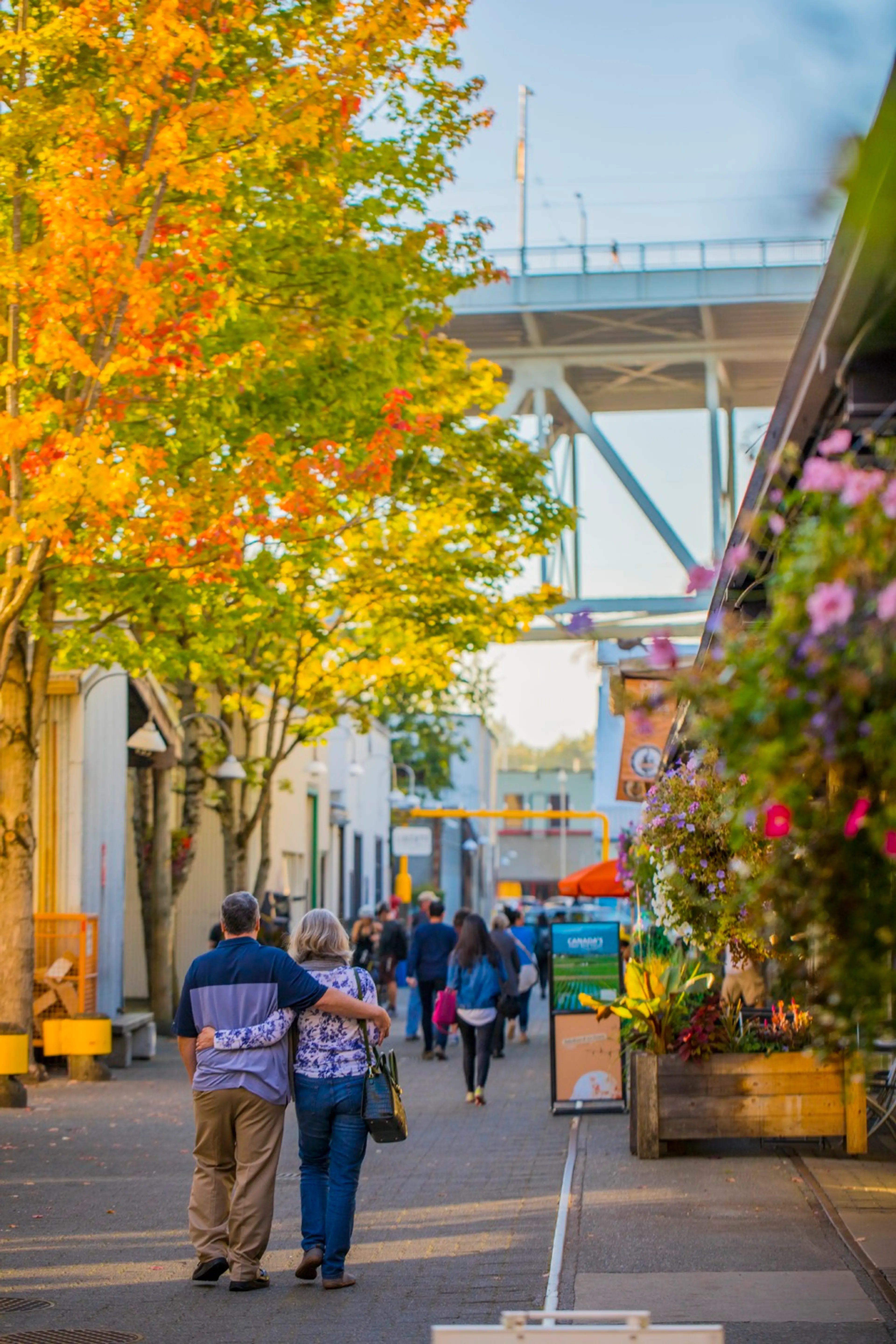 People walk past trees with fall colours on Granville Island in Vancouver