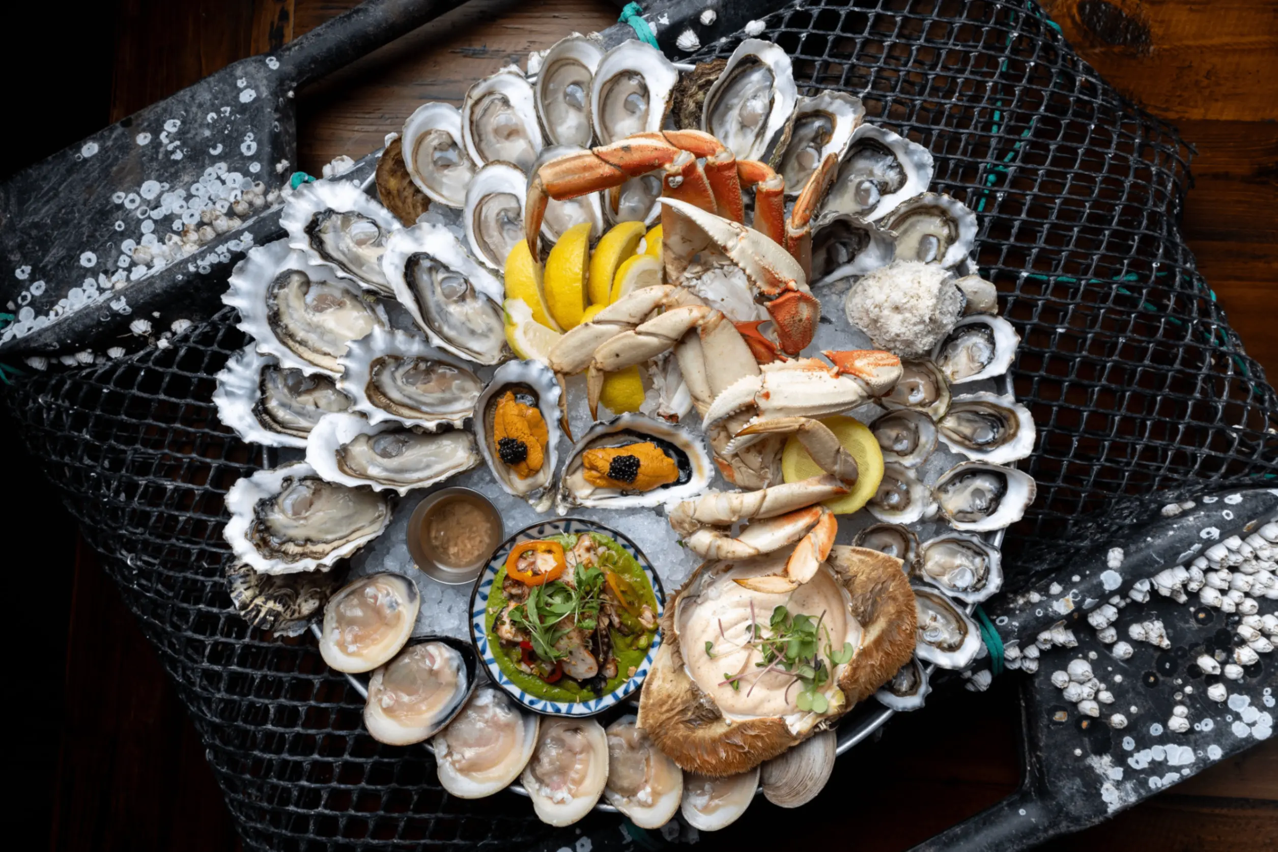 Seafood platter with crab claws, oysters, clams, lemon wedges, and dipping sauces on a bed of ice.