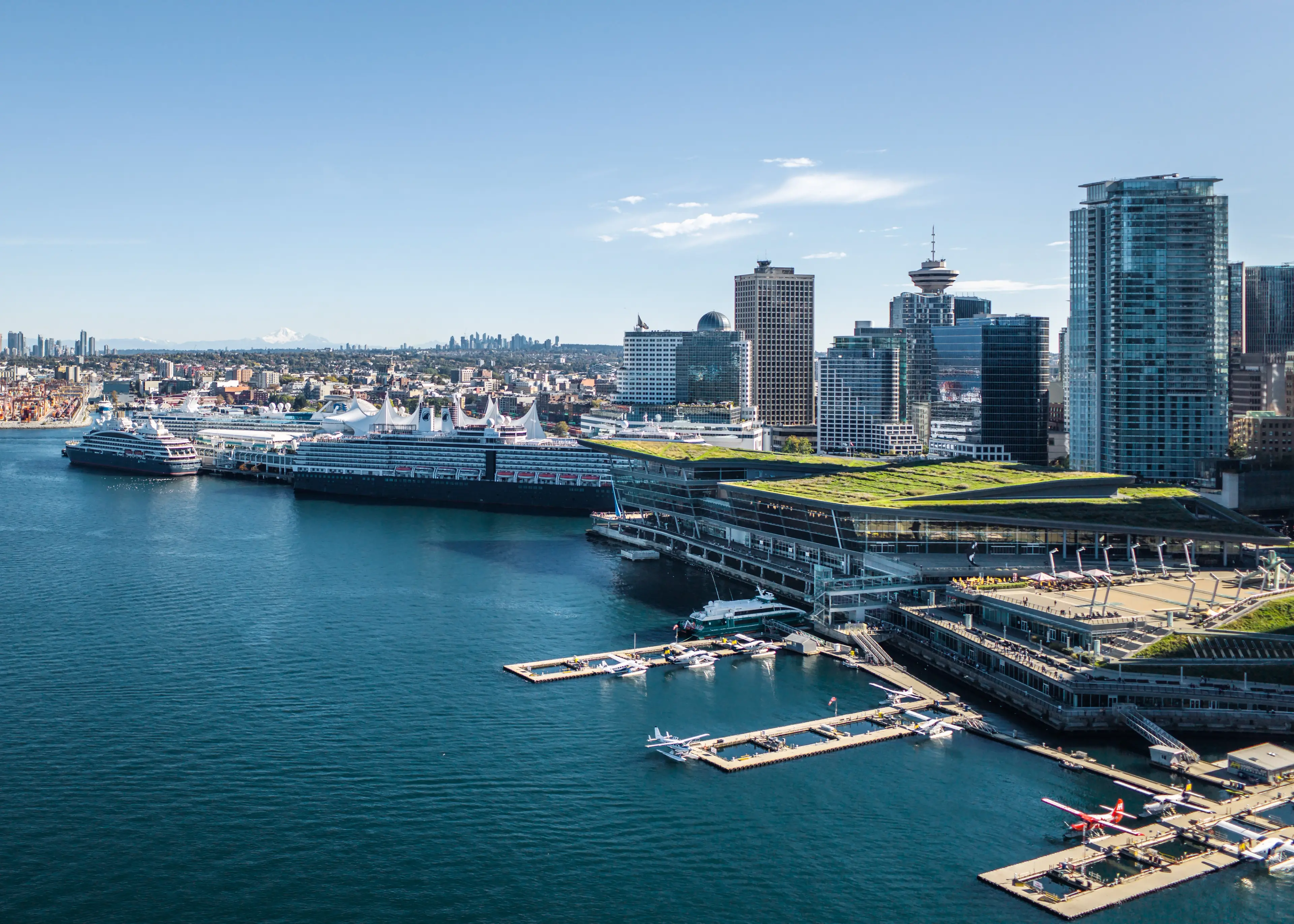 City skyline with tall buildings and cruise ships docked at a waterfront terminal under a clear blue sky.