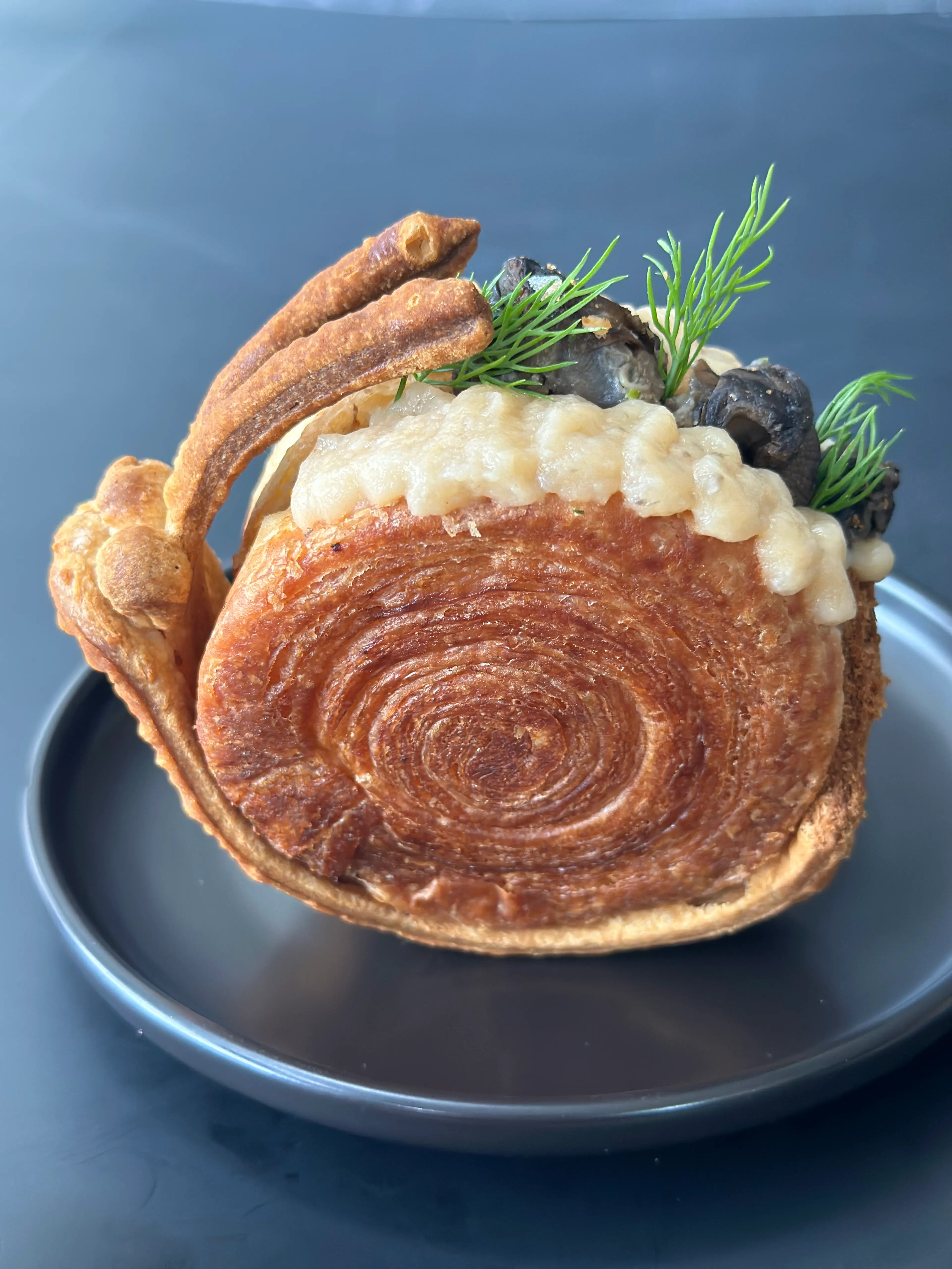 A La Mode's Bourguignon Escargot Spiral Croissant Pie, styled in rhe shape of a snail, with escargots topping its back. 