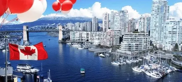 Red and white balloons and a Canadian flag over a harbor with boats and a city skyline with a bridge and mountains in the background.