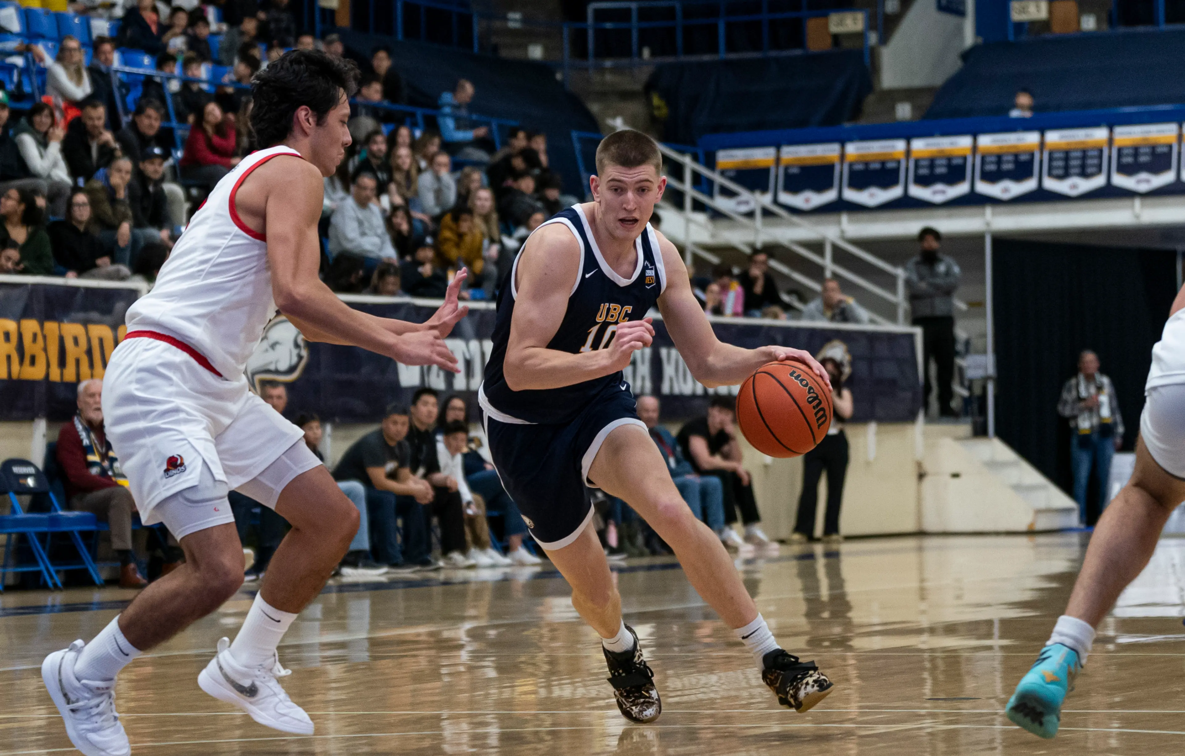 Two men play basketball at UBC in front of a crowd. 