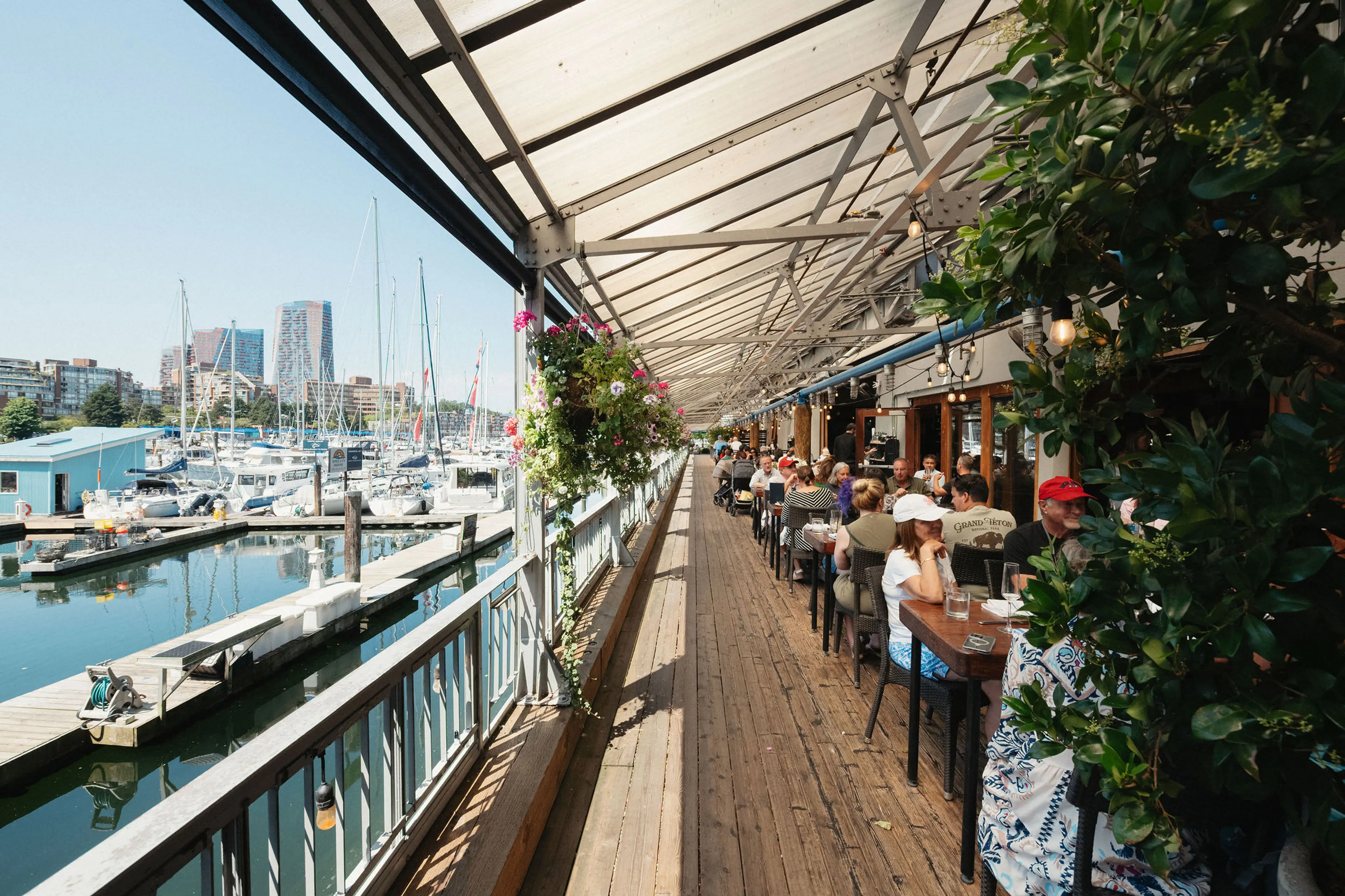 Outdoor restaurant seating along a marina with boats docked and people dining under a covered wooden deck.