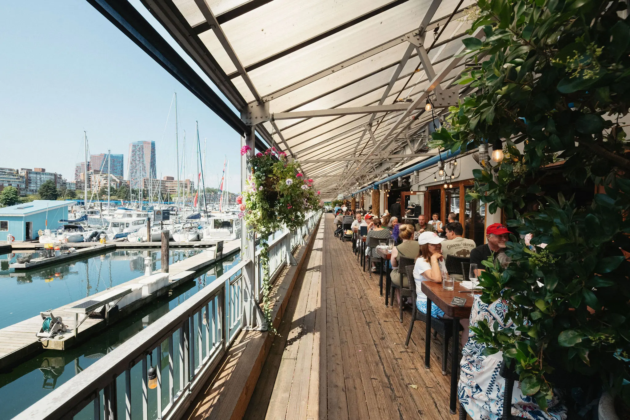 Outdoor restaurant seating along a marina with boats docked and people dining under a covered wooden deck.