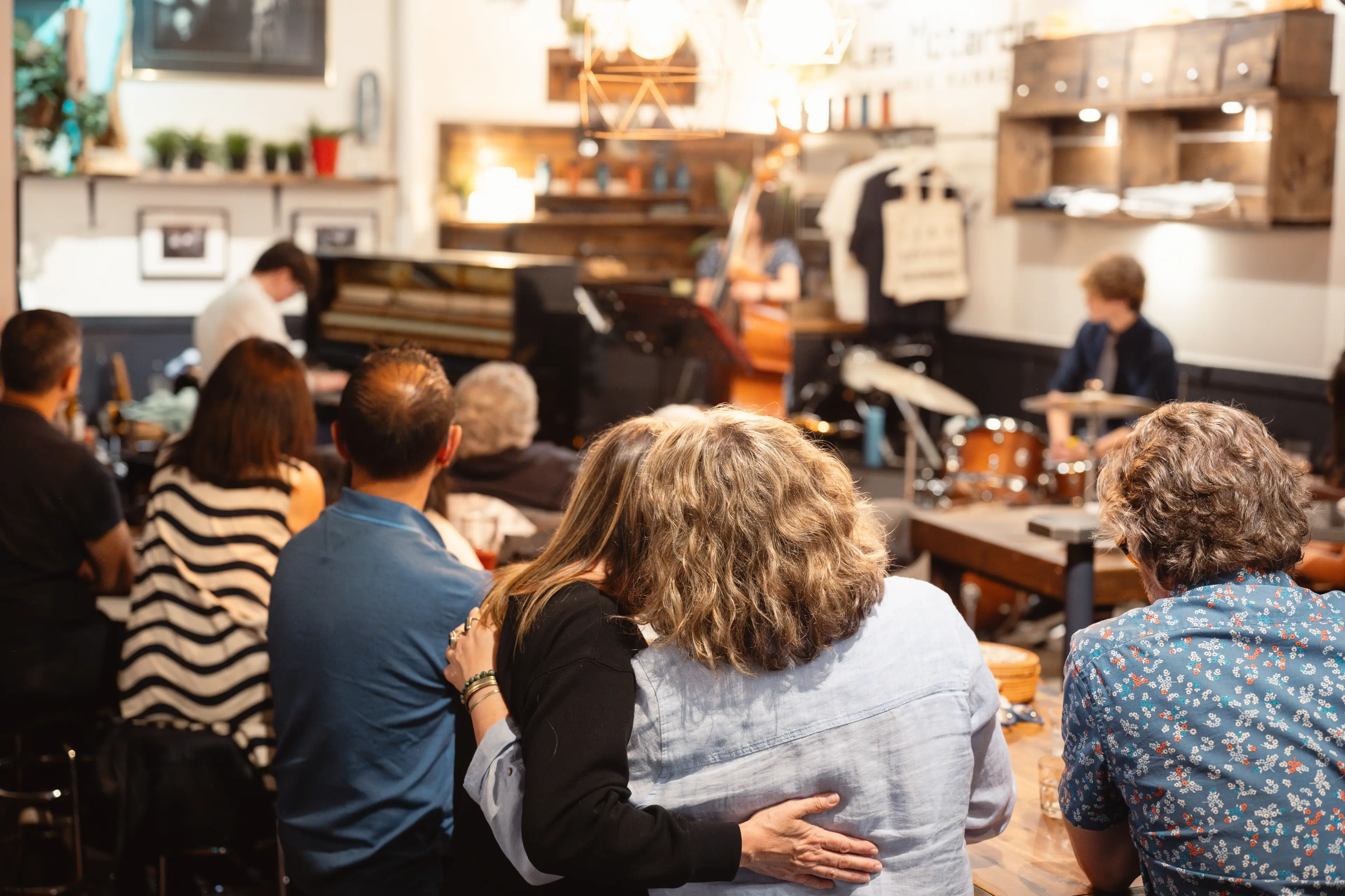 Audience seated and watching a live music performance with a pianist and drummer in a cozy indoor venue.