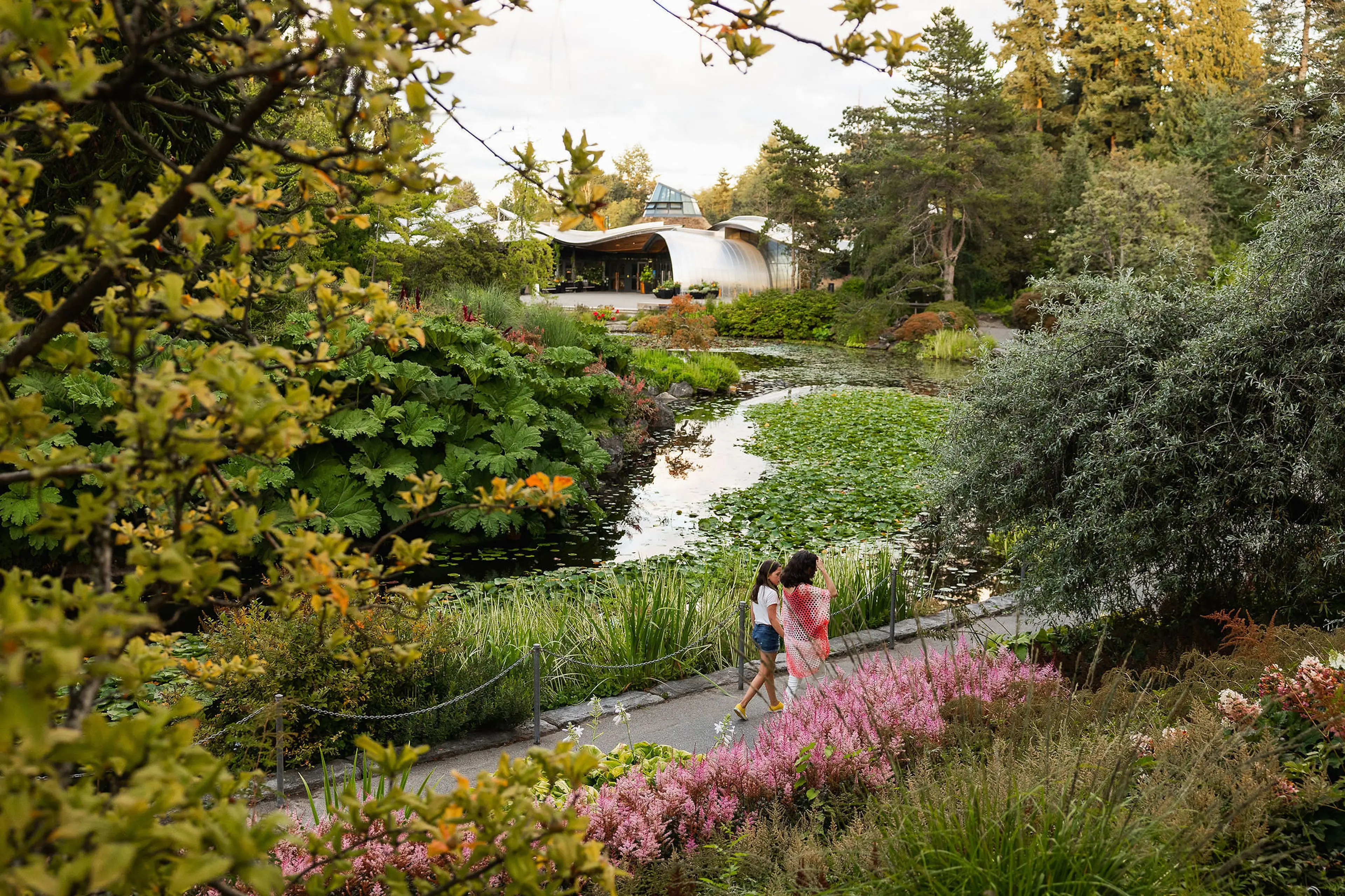 A woman and child walk through a blooming garden past a lily-covered pond at VanDusen Botanical Garden in Vancouver.