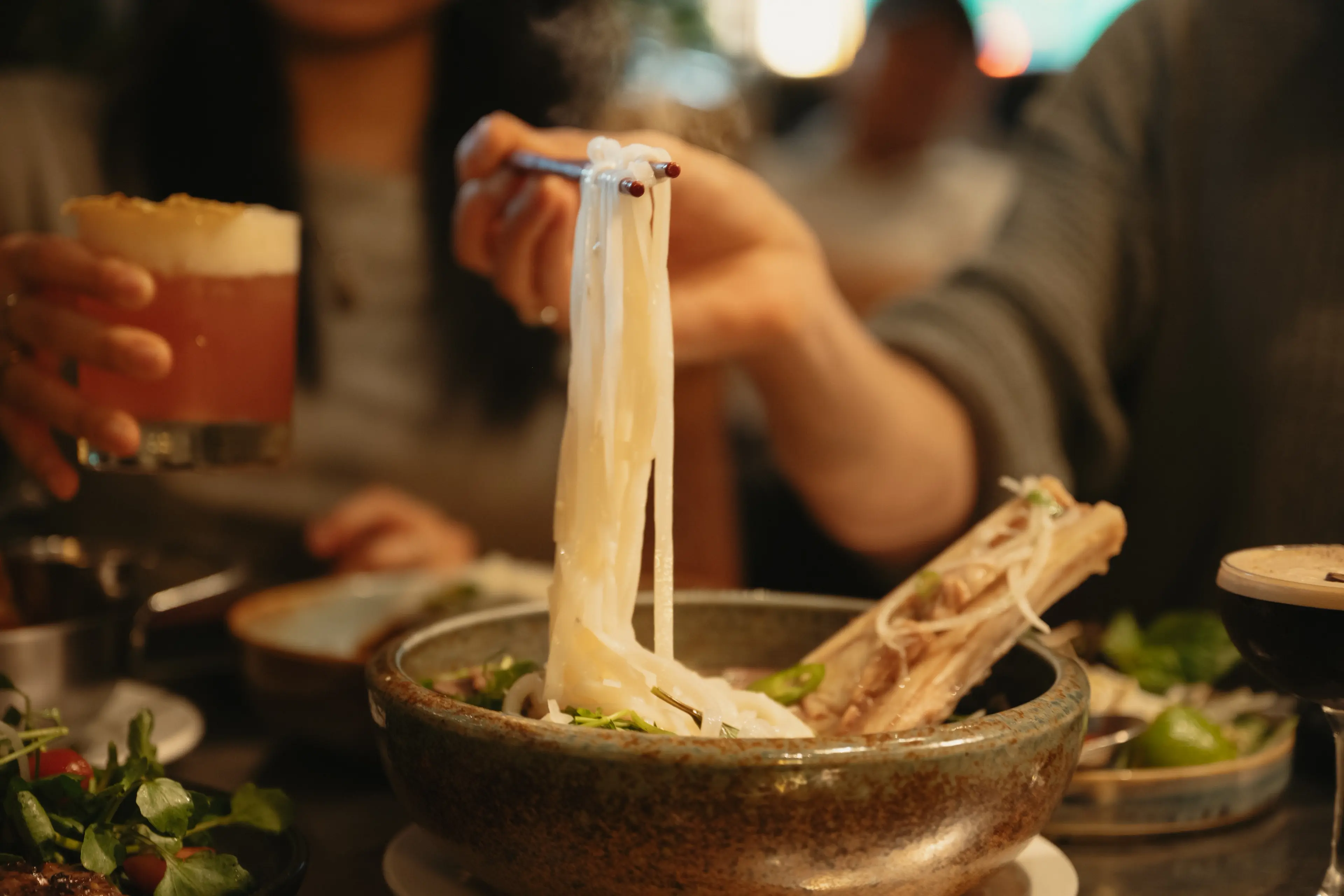 A bowl of pho with a hand pulling out the noodles at the Lunch Lady in Vancouver.