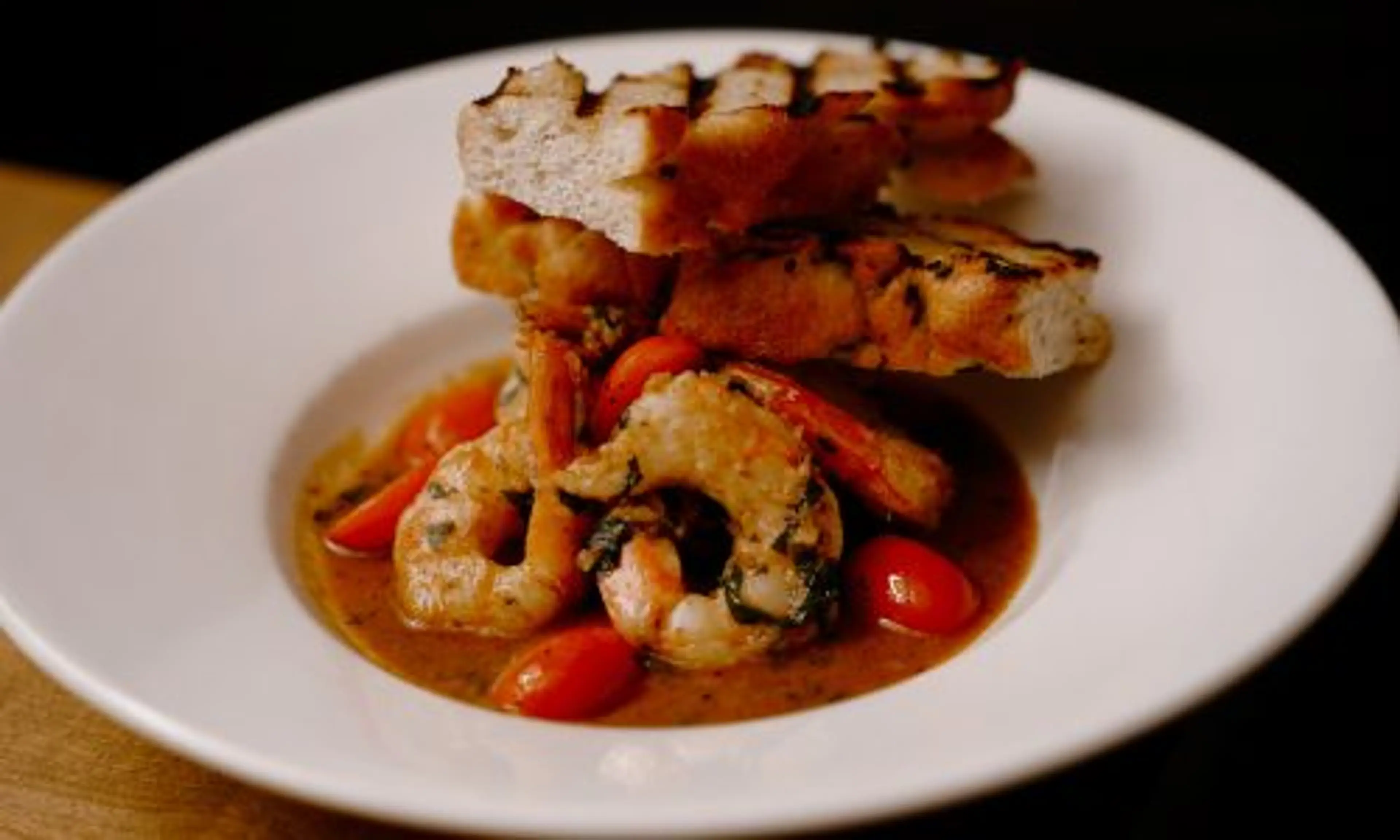 Shrimp in sauce with cherry tomatoes served in a white bowl topped with grilled bread slices.
