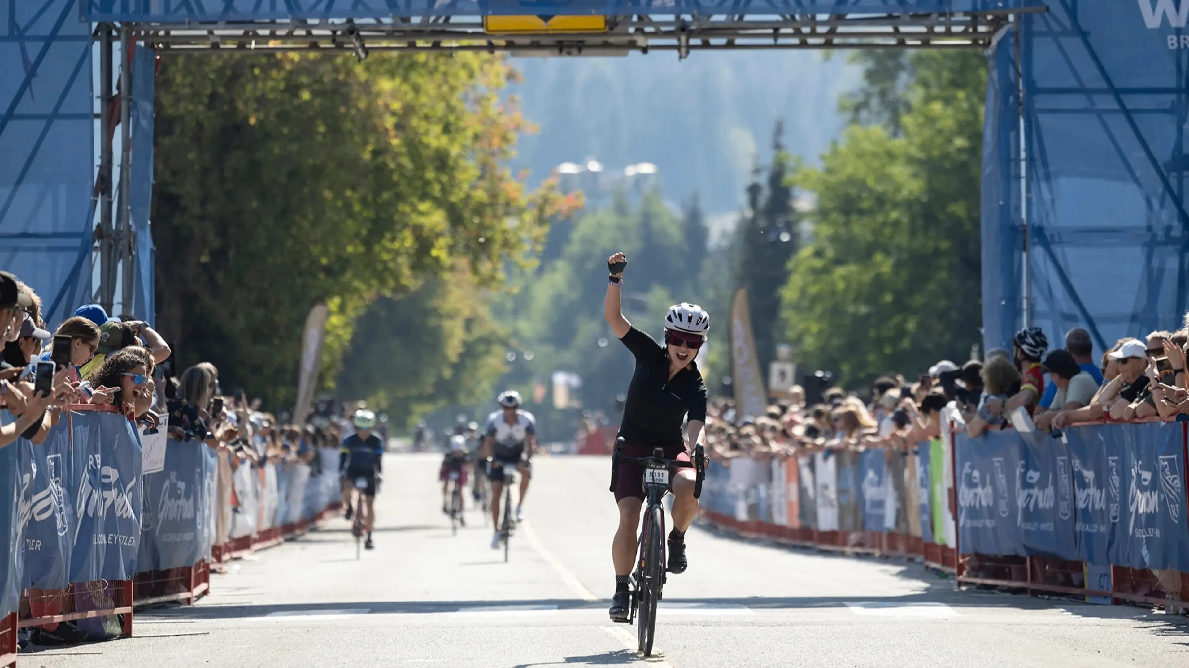 Cyclist raising a fist in celebration while crossing the finish line of a race with spectators on both sides.