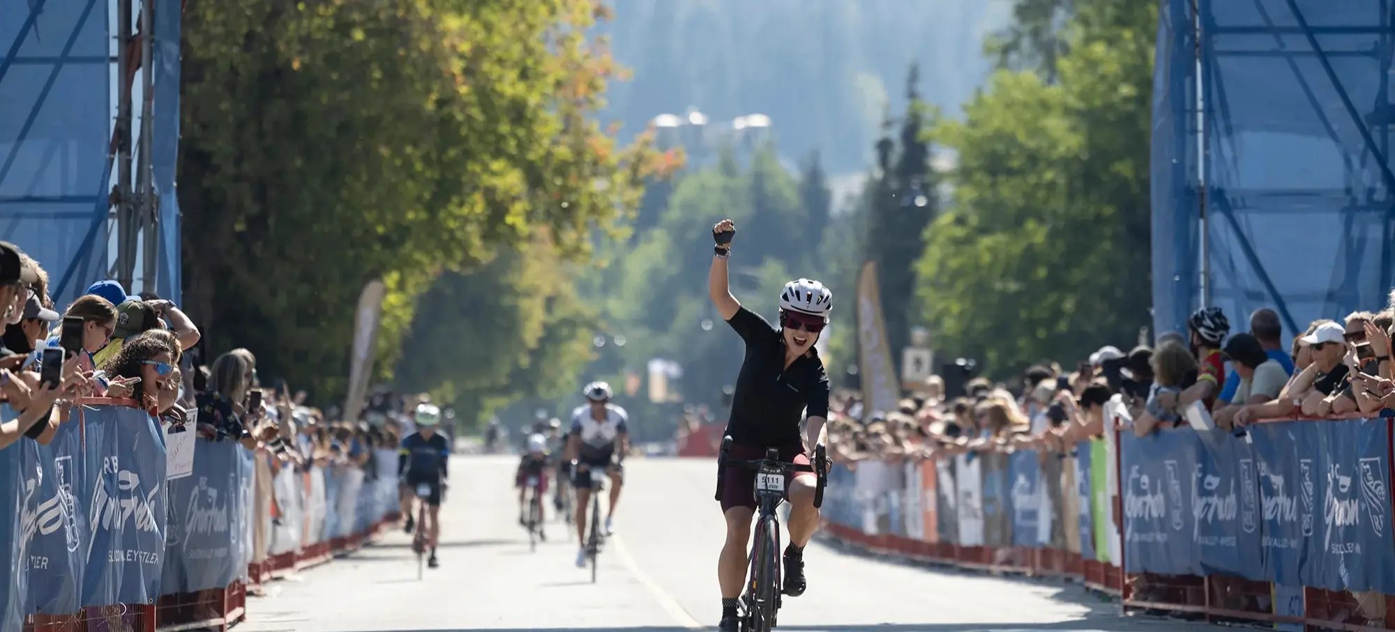 Cyclist raising a fist in celebration while crossing the finish line of a race with spectators on both sides.