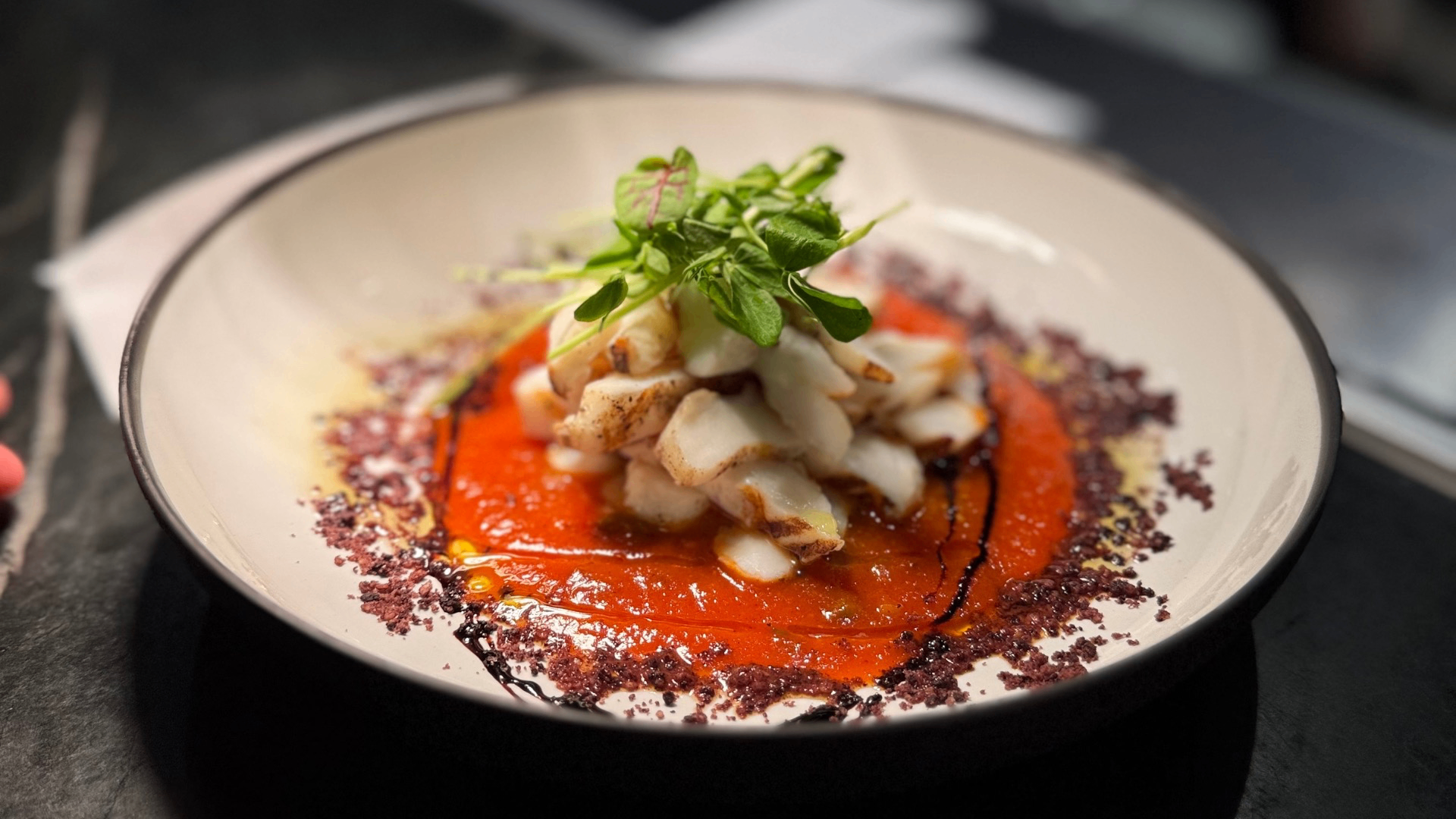 Grilled white fish pieces on red sauce garnished with green herbs and sprinkled with purple seasoning on a white plate.