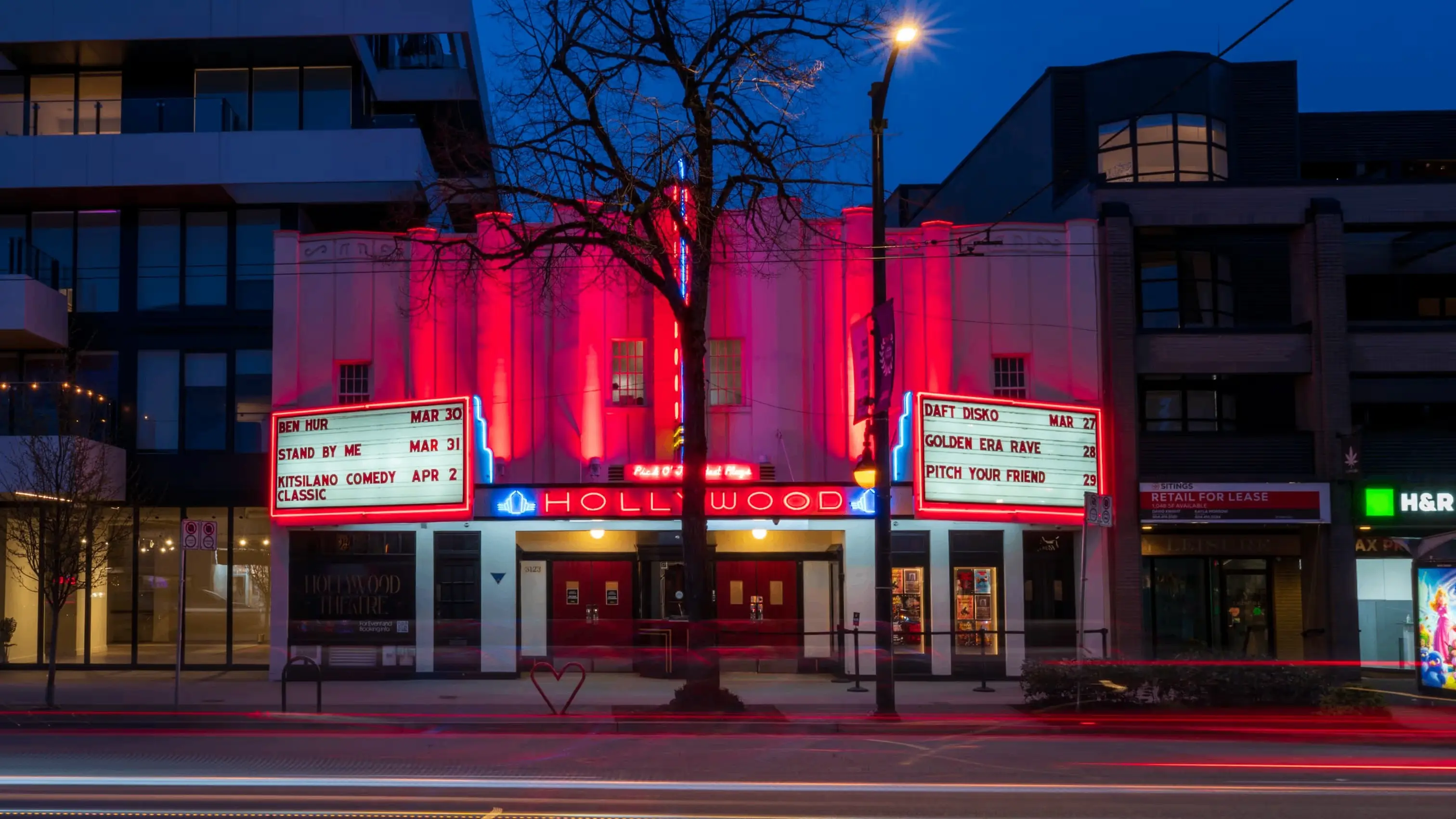 Historic Hollywood Theatre lit with red neon lights at night, showing movie titles and dates on marquees.