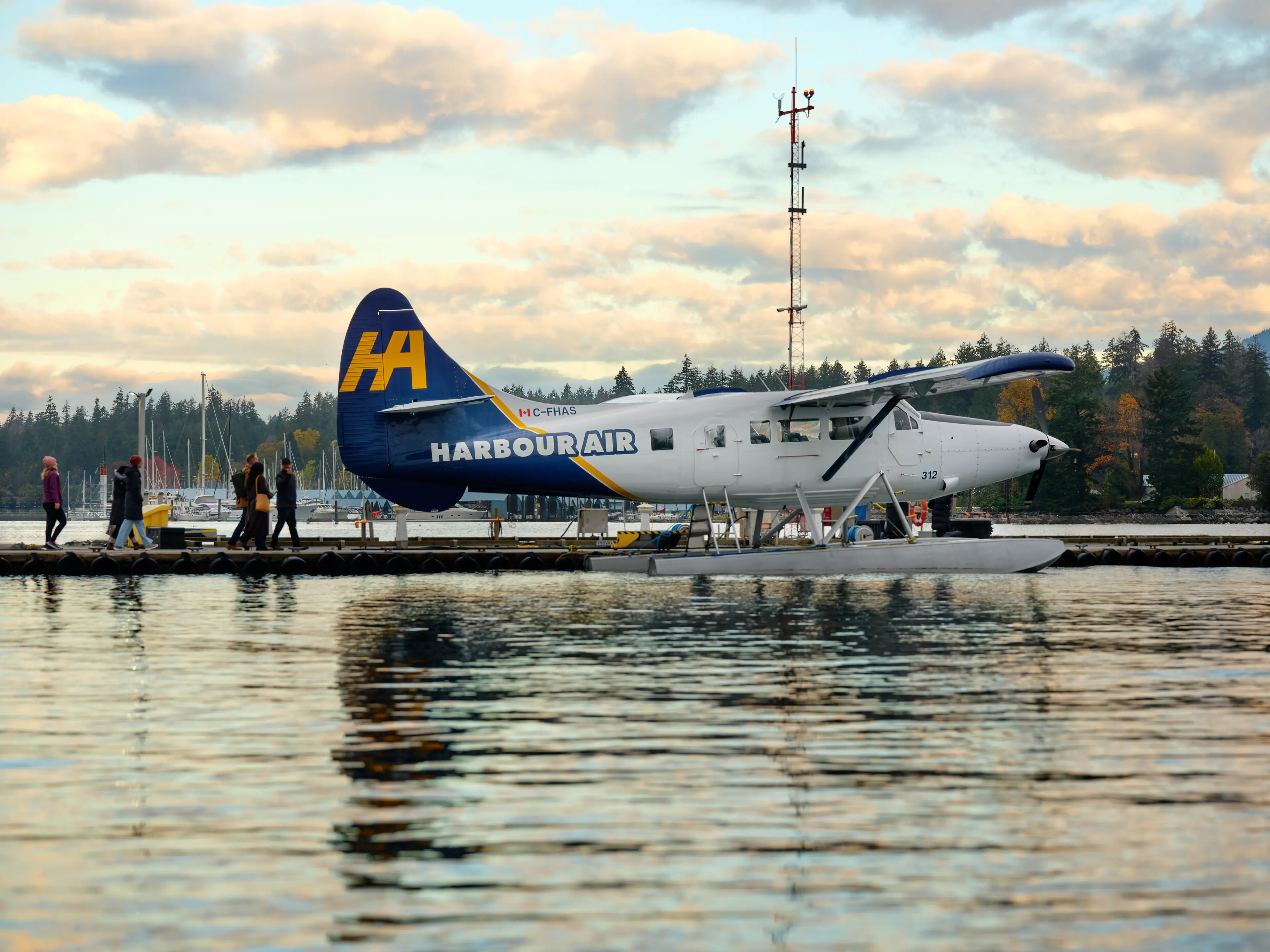 A Harbour Air seaplane docked at the departure terminal with a forested backdrop and a glowing morning sky.
