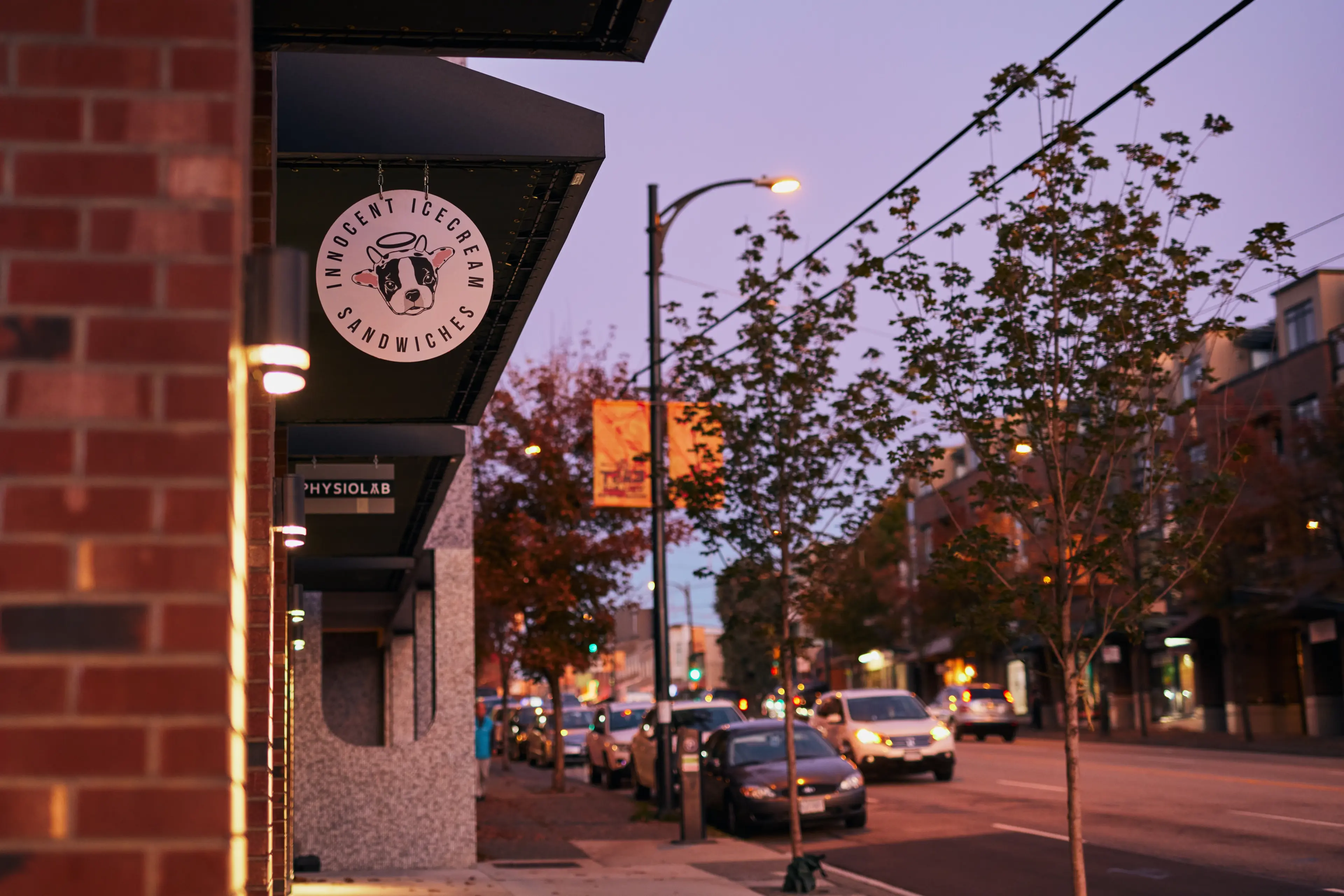 Street view at dusk with a sign reading 'Innocent Ice Cream Sandwiches' featuring a dog's face.