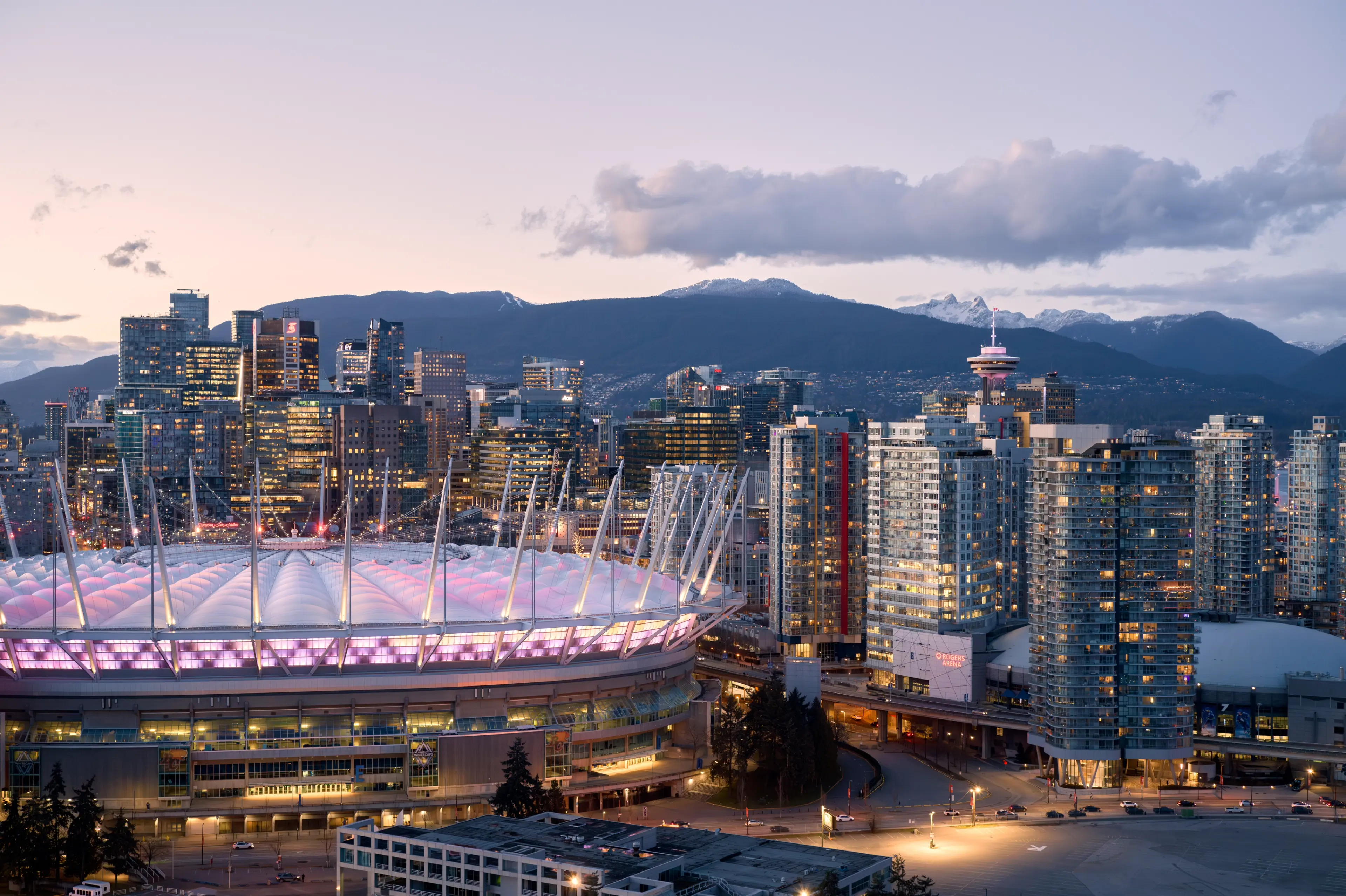 BC Place in the dusk surrounded by high-rises and snow covered mountains in the background