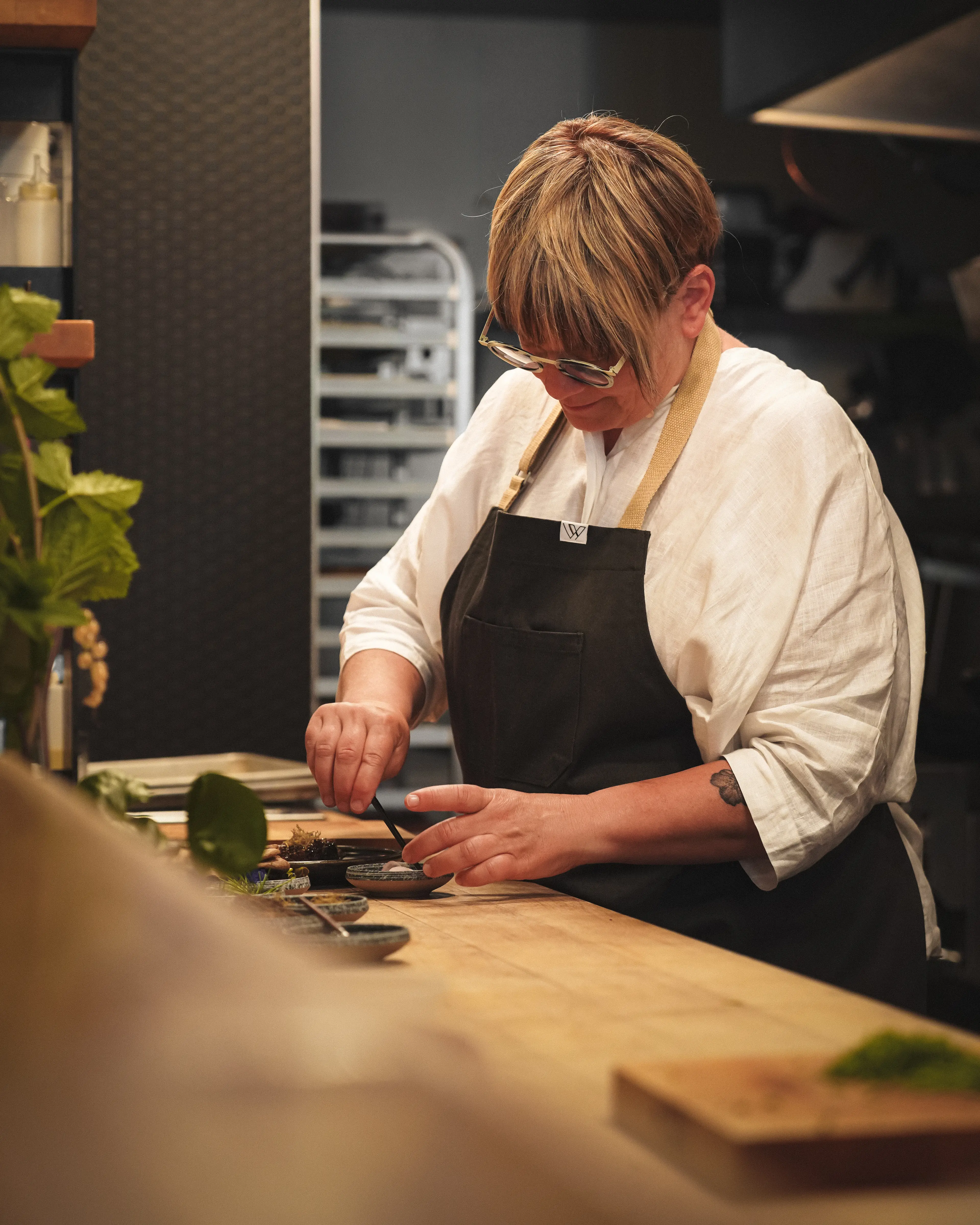 Person wearing glasses and apron preparing food at a wooden counter in a kitchen.