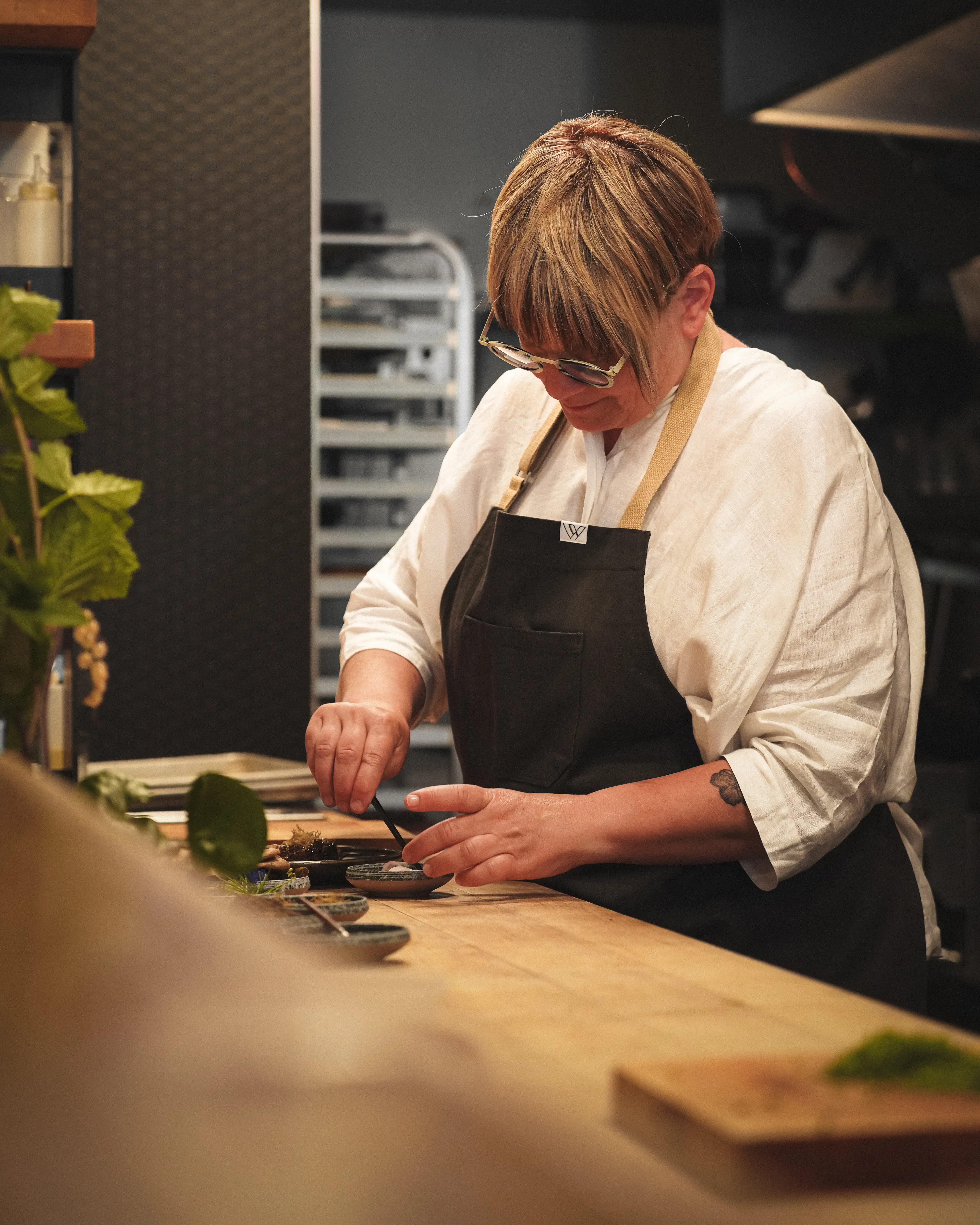 Person wearing glasses and apron preparing food at a wooden counter in a kitchen.