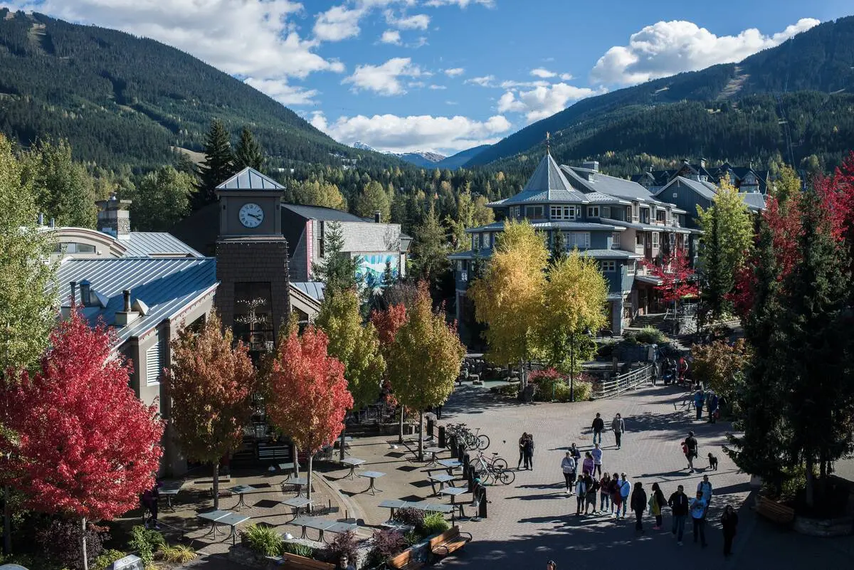 Wide shot of Whistler Village on a sunny day with trees in fall colours.