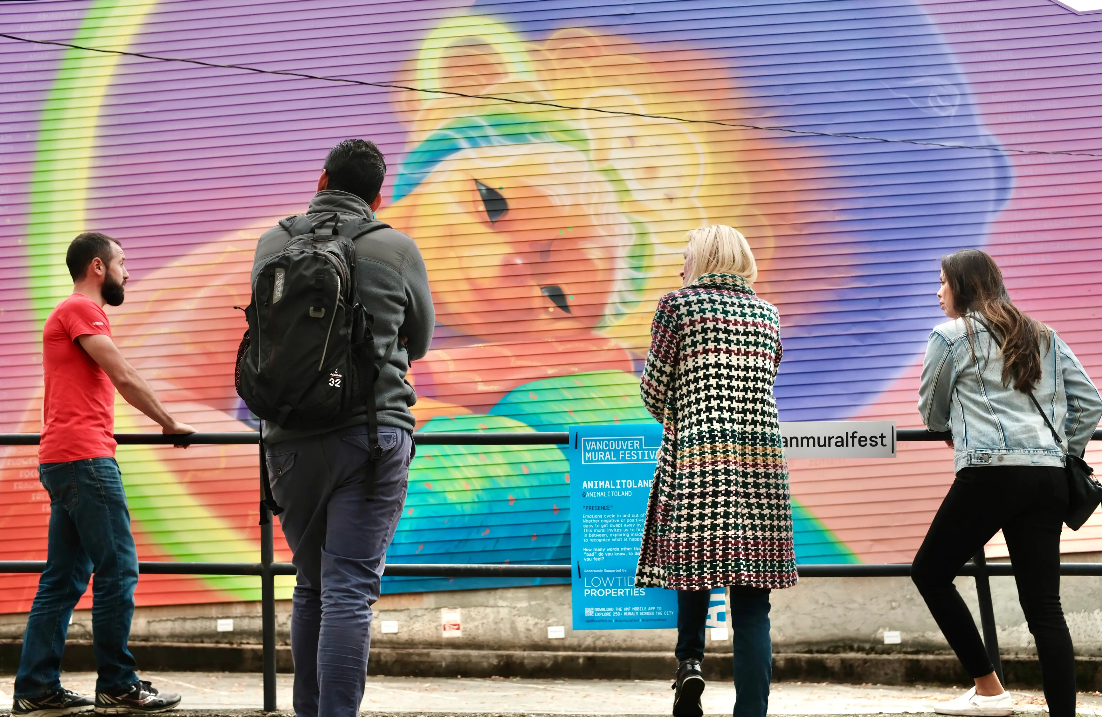 Four people standing and looking at a colorful mural of a bear on a wall during a guided tour.