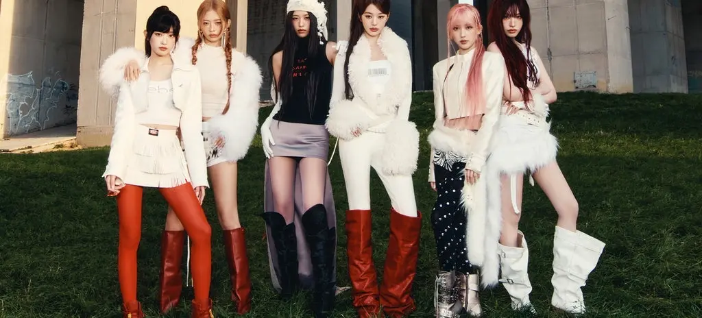 Six people standing on grass in front of a concrete structure, wearing stylish outfits with boots and fur accents.
