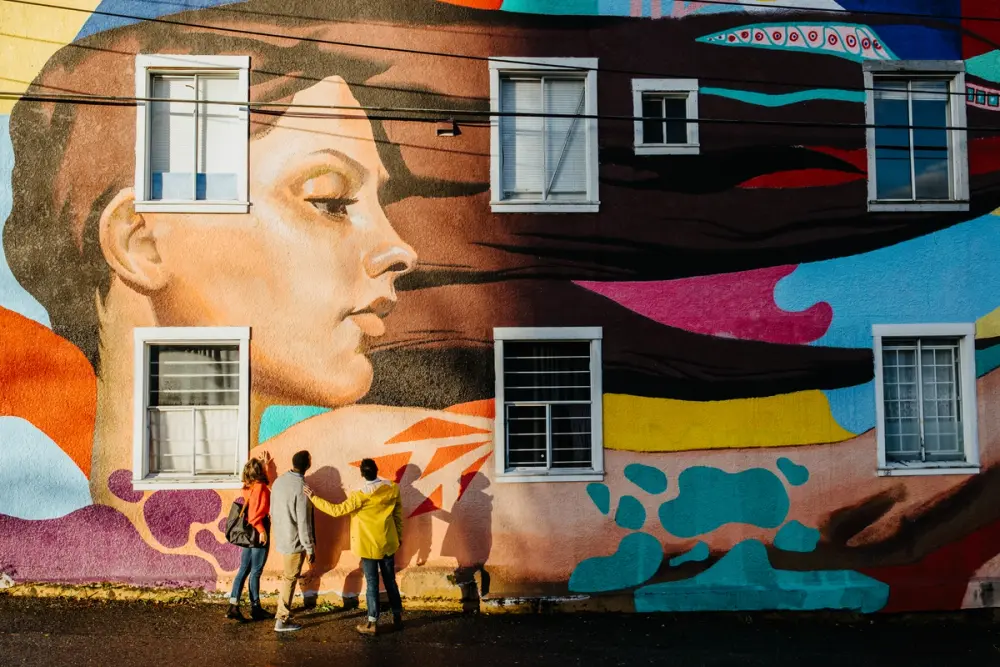 Three people stand beneath a large colourful mural depicting a woman