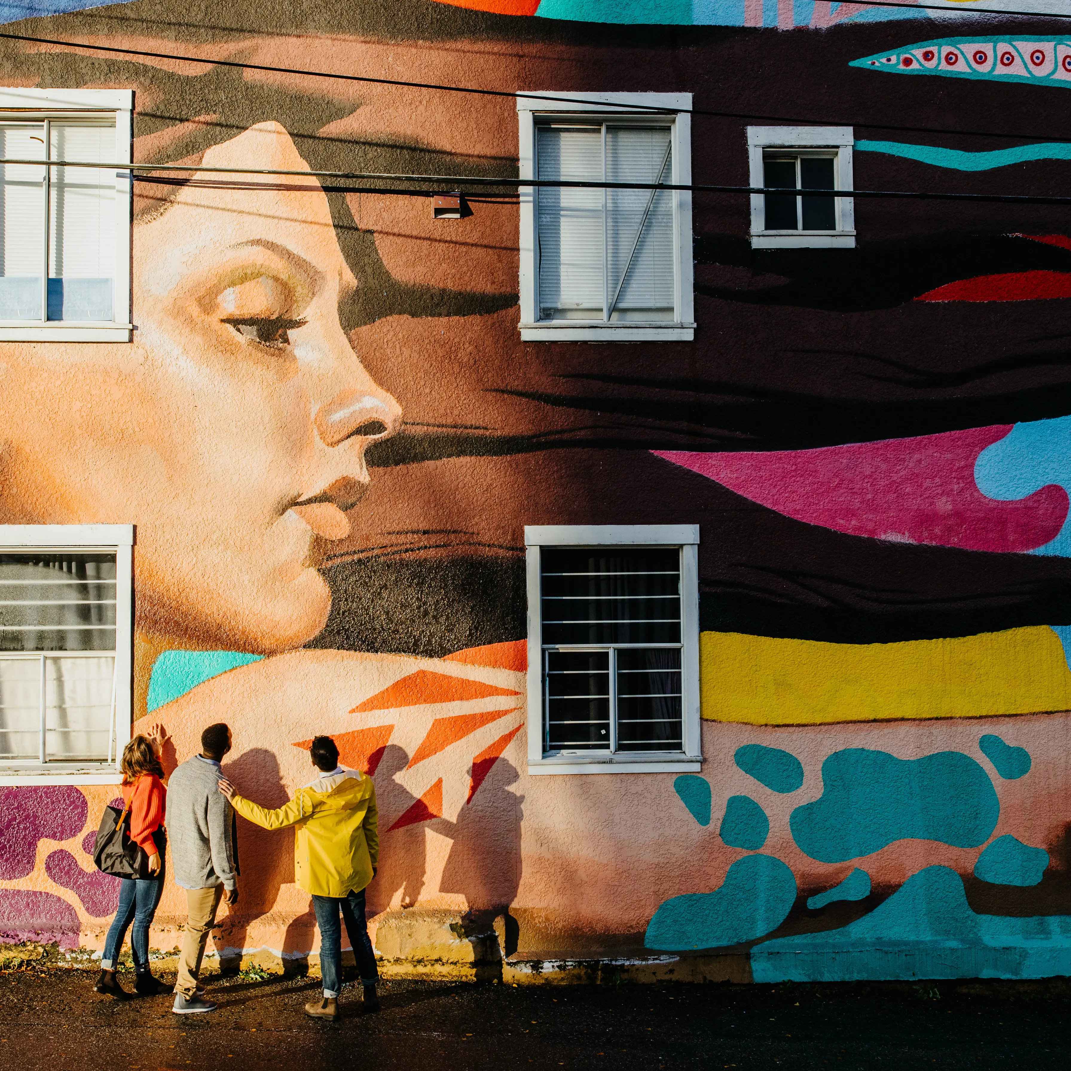 Three people stand beneath a large colourful mural depicting a woman