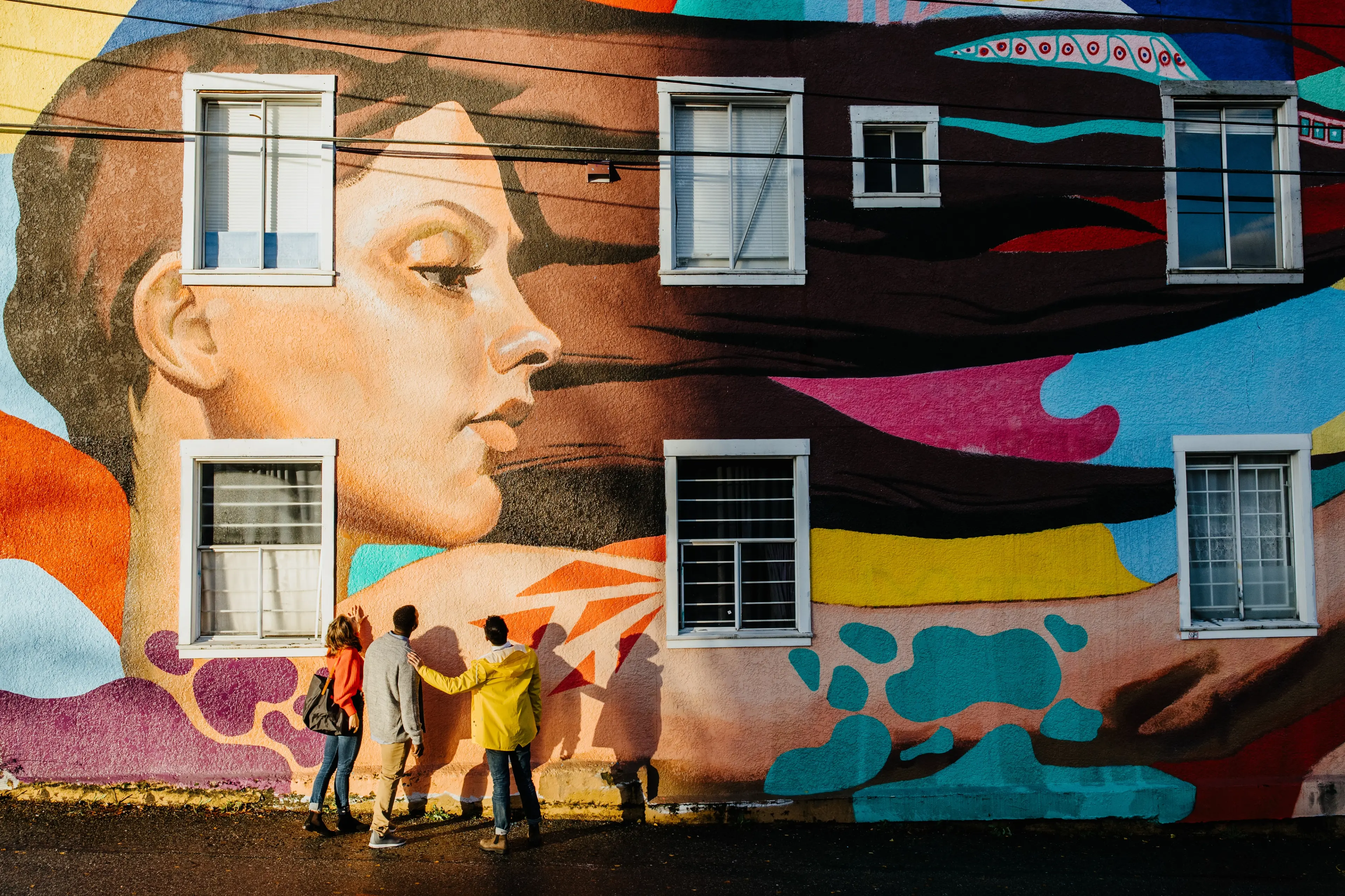 Three people stand beneath a large colourful mural depicting a woman