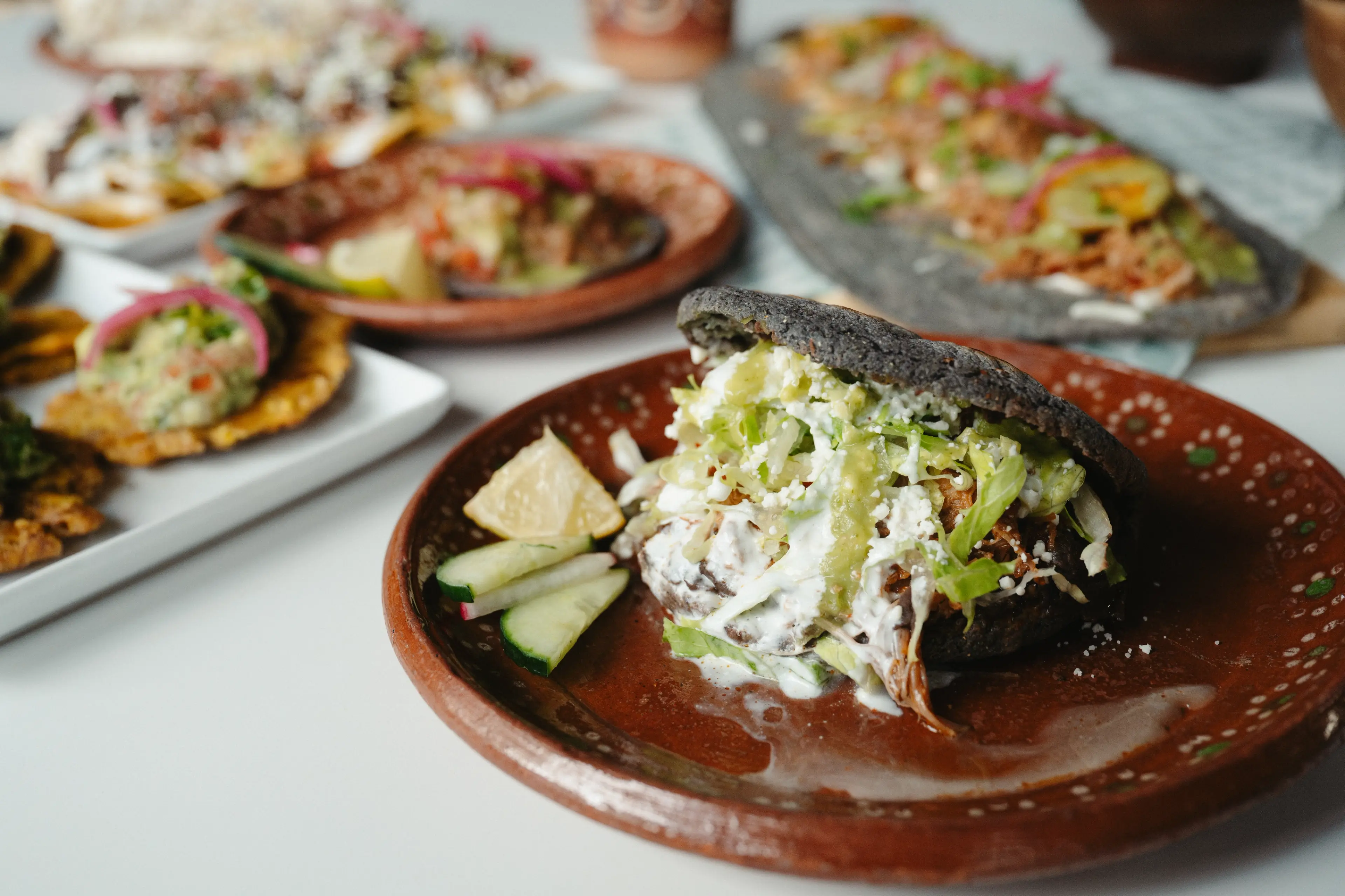 Torta sandwich with black bread filled with shredded meat, lettuce, cheese, and sauce on a brown plate with cucumber slices and a lemon wedge.