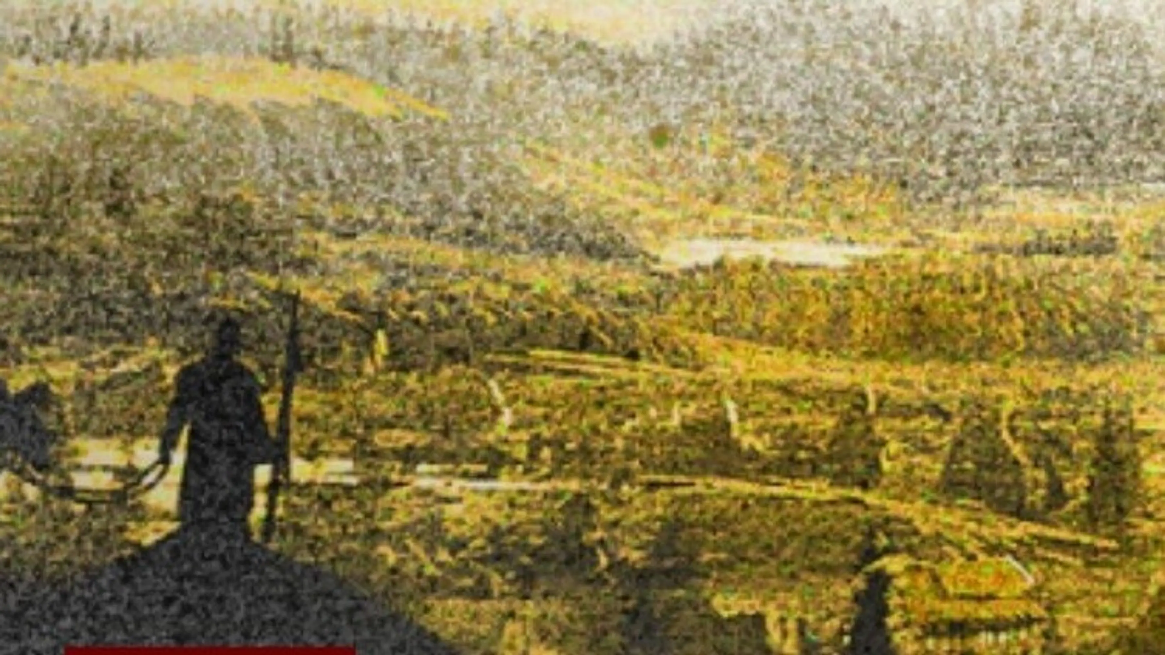 Silhouette of a person holding a rifle overlooking a vast, yellow-tinted landscape with hills and scattered buildings.