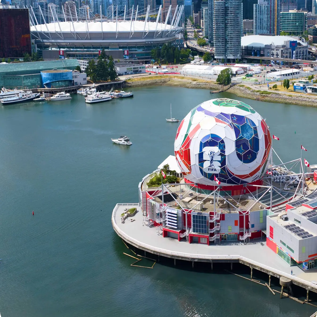 Waterfront cityscape with a large colorful spherical building featuring FIFA 2026 logo and boats on the water.