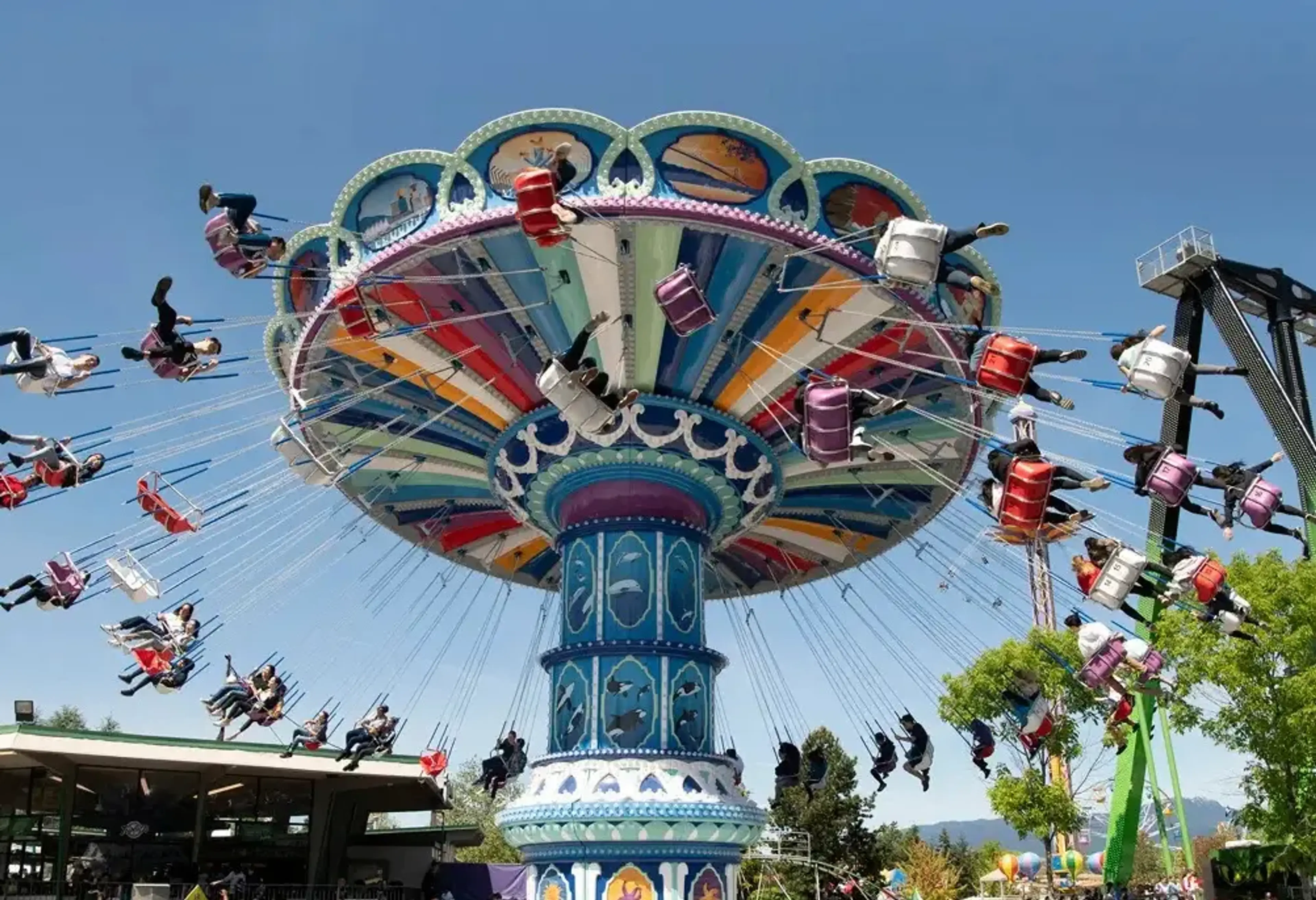 Colorful swing ride at an amusement park with many people seated and spinning against a clear blue sky.