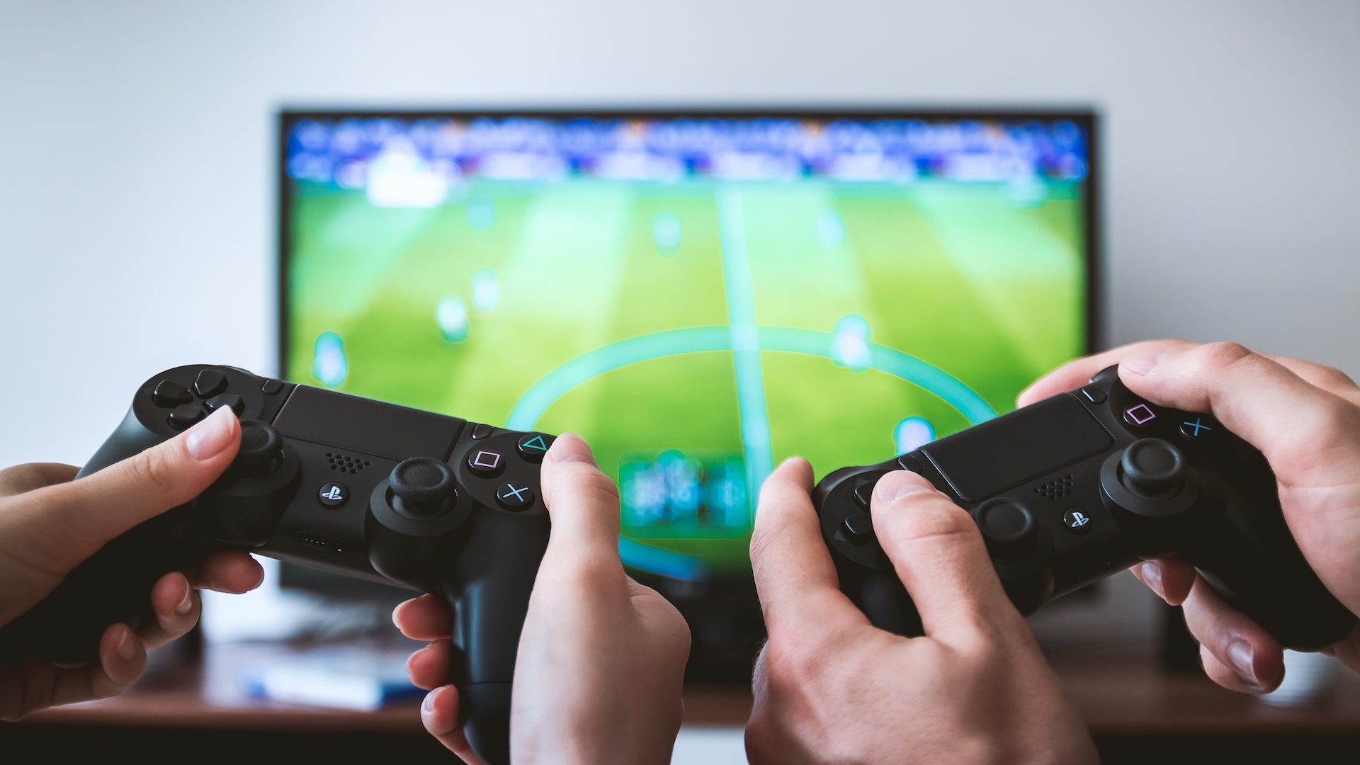 Two people hold game controllers in front of a soccer video game
