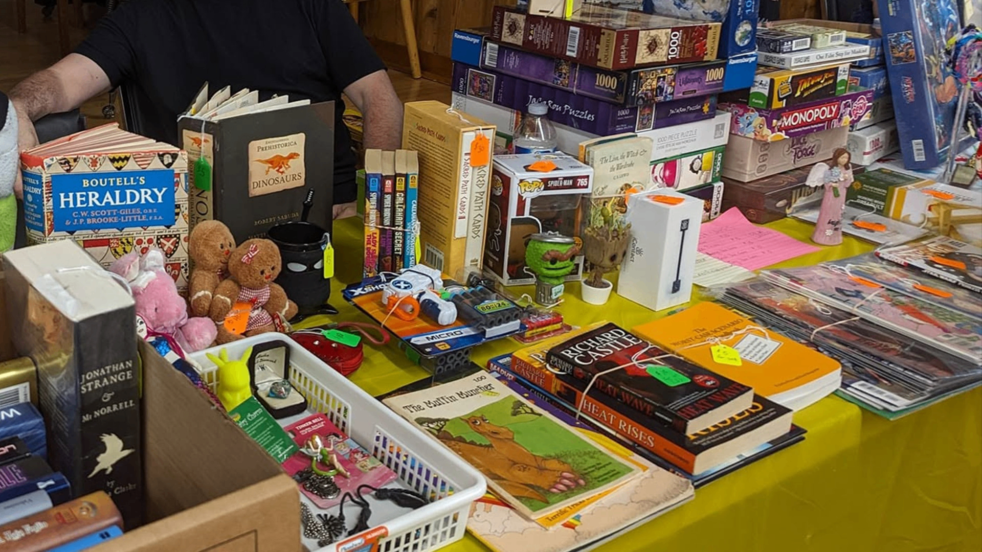 Table with books, board games, toys, and collectibles for sale at a market or fair.