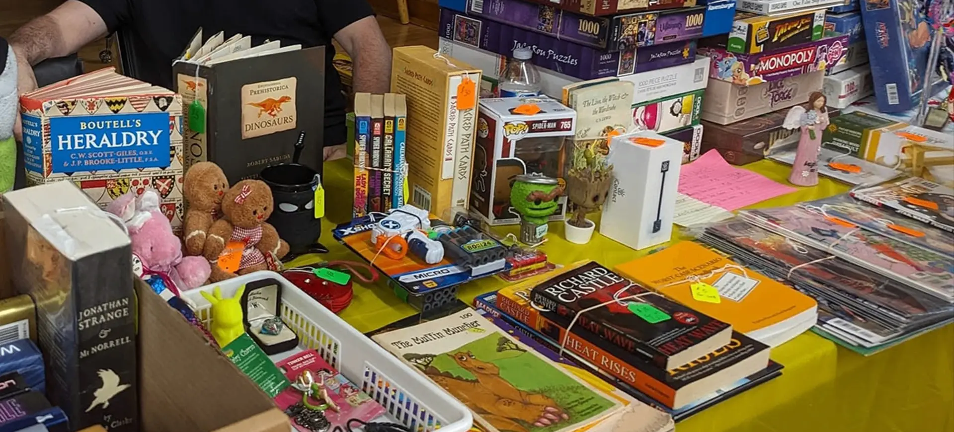 Table with books, board games, toys, and collectibles for sale at a market or fair.