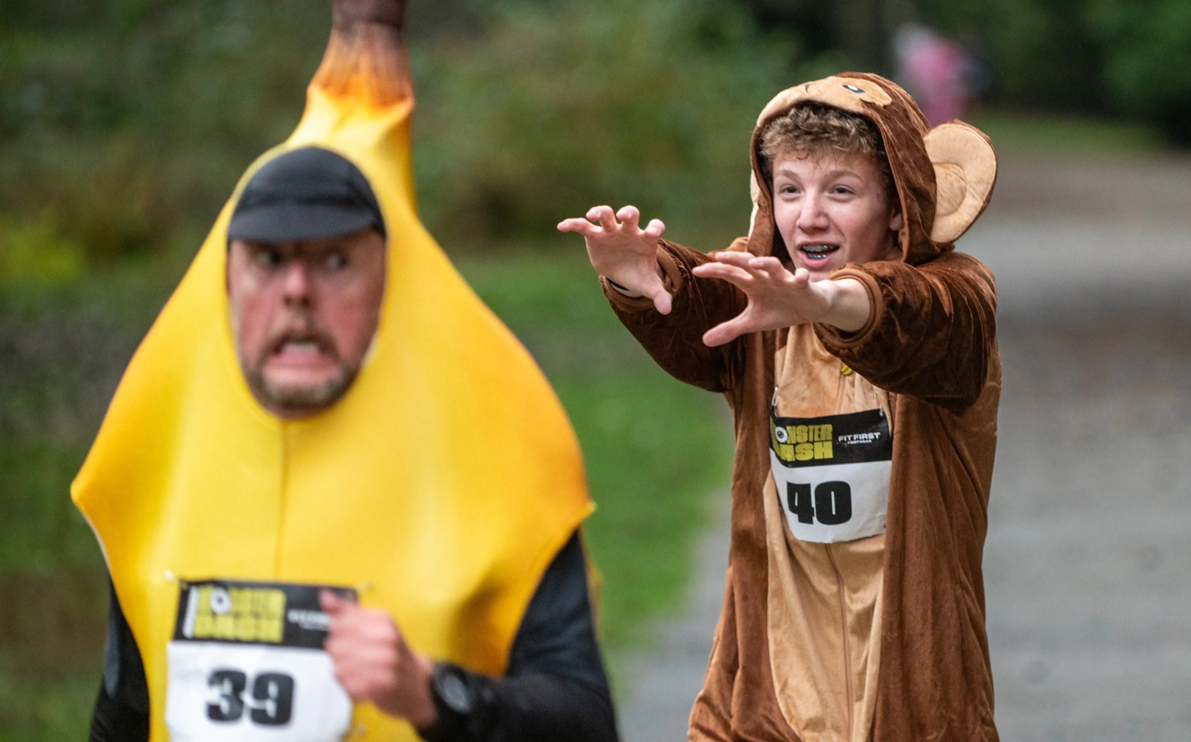 Two people in costumes running outdoors, one in a banana costume and the other in a monkey costume reaching forward.