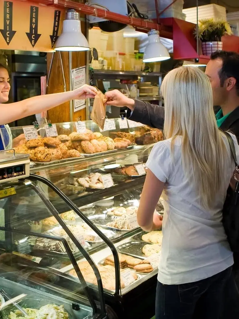 A woman is serving customers at a busy deli and bakery in a public market