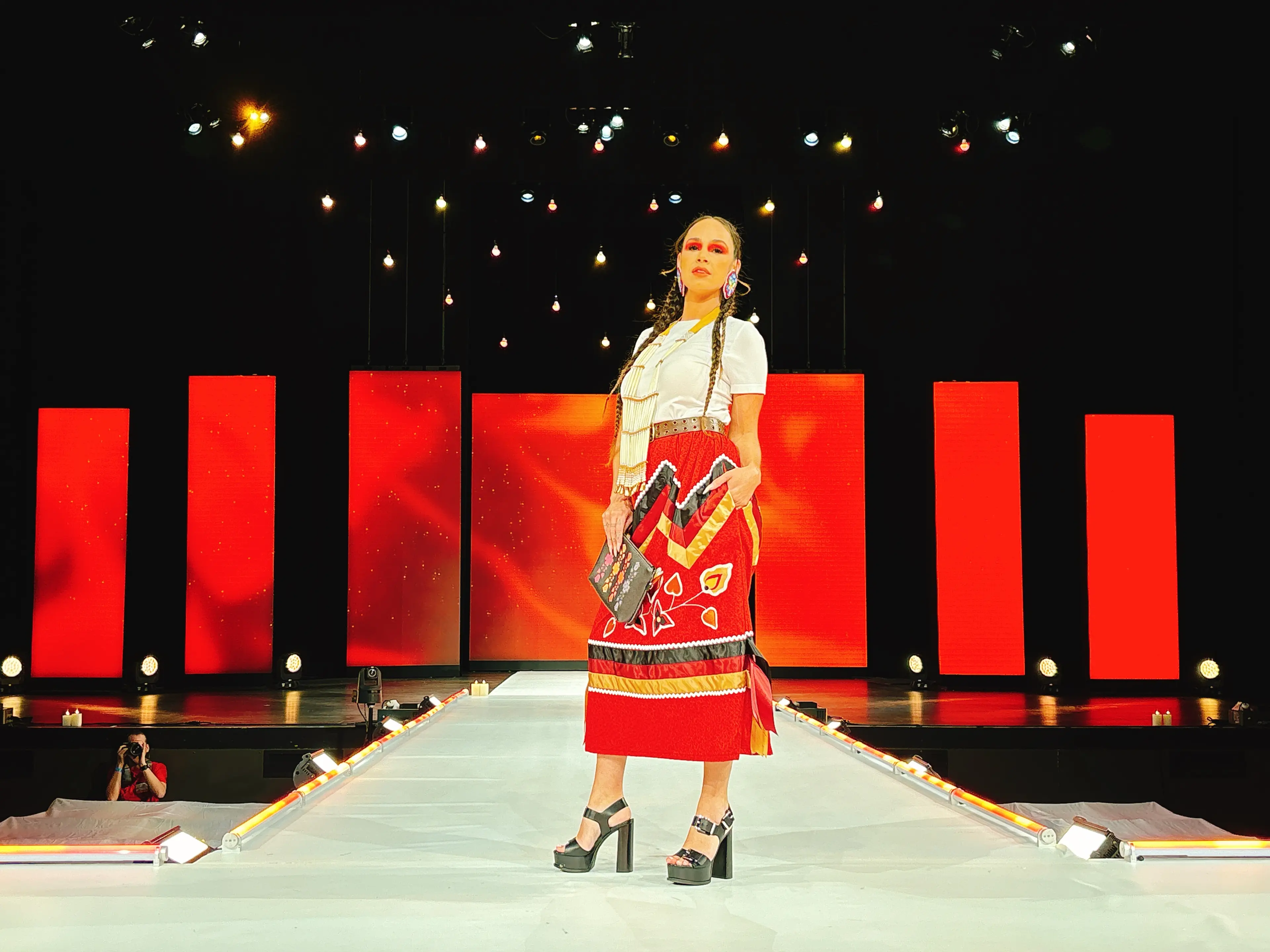 A model wearing a red ribbon skirt and holding a clutch by Ocean Kiana poses on the VIFW runway