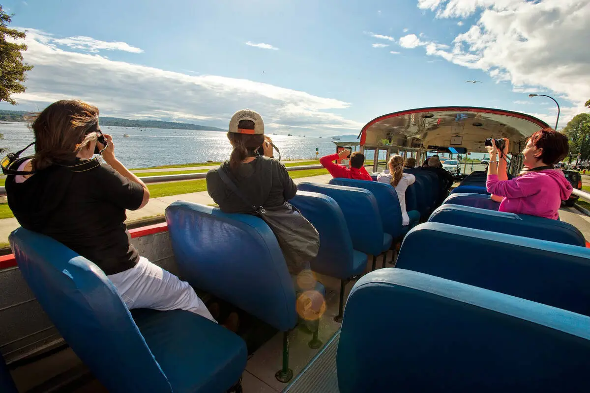 People take photos of English Bay from a hop-on, hop-off bus