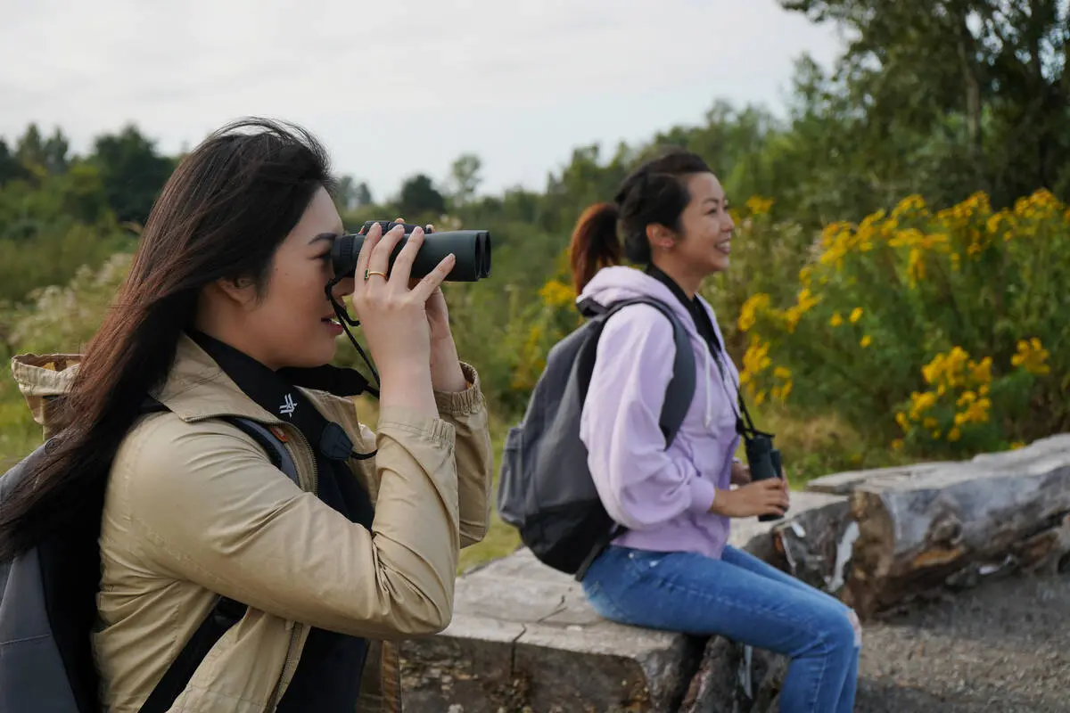 Two women hold binoculars and watch for birds.