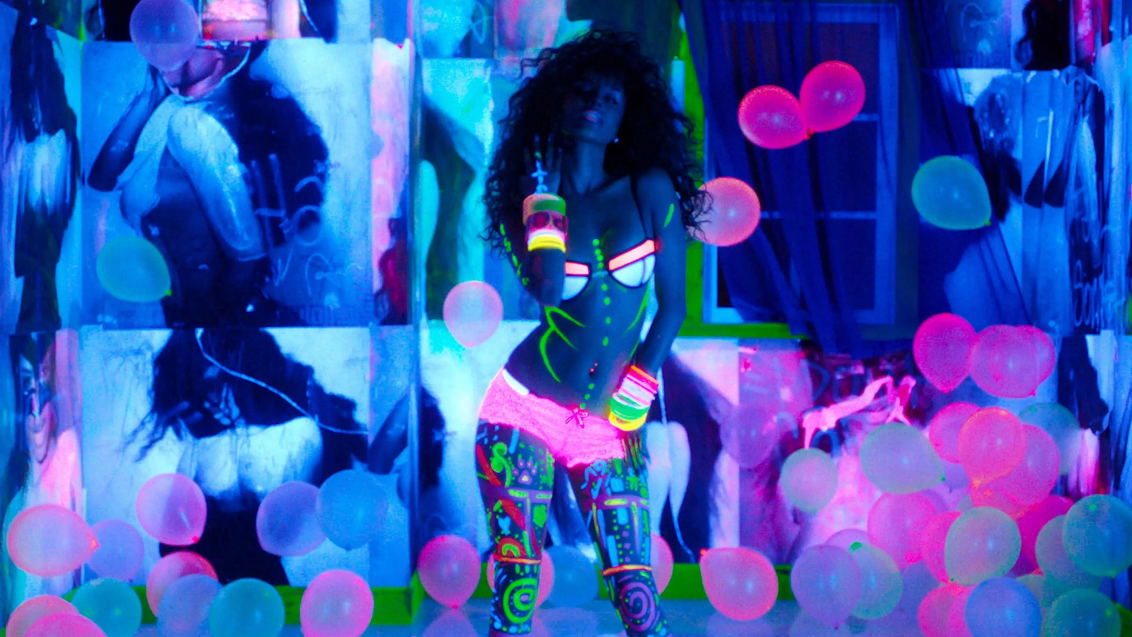 Person in neon body paint and glowing lingerie dancing among pink and blue balloons in a room with blacklight and artistic wall posters.