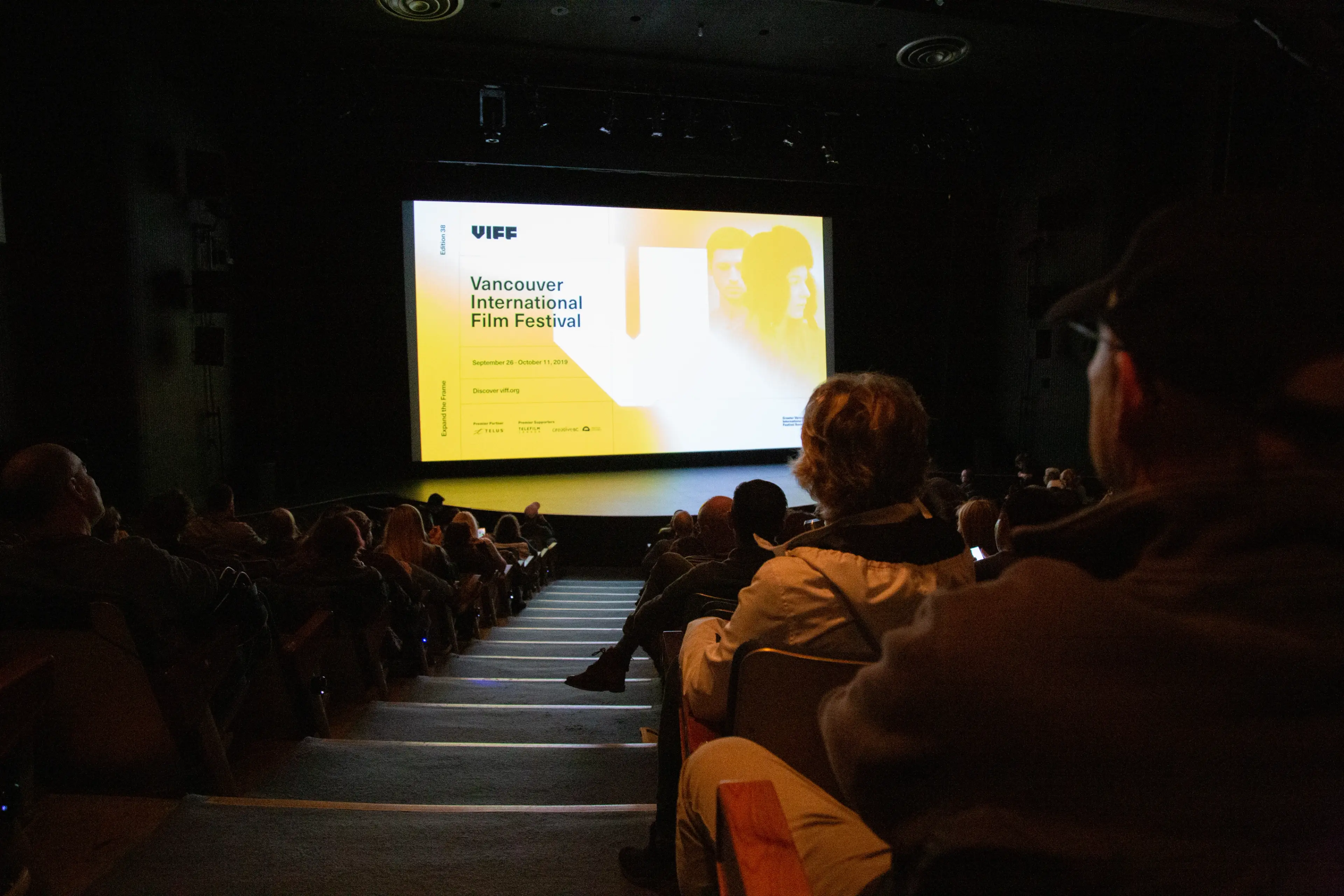 Audience seated in a dark theater watching a screen displaying Vancouver International Film Festival information.