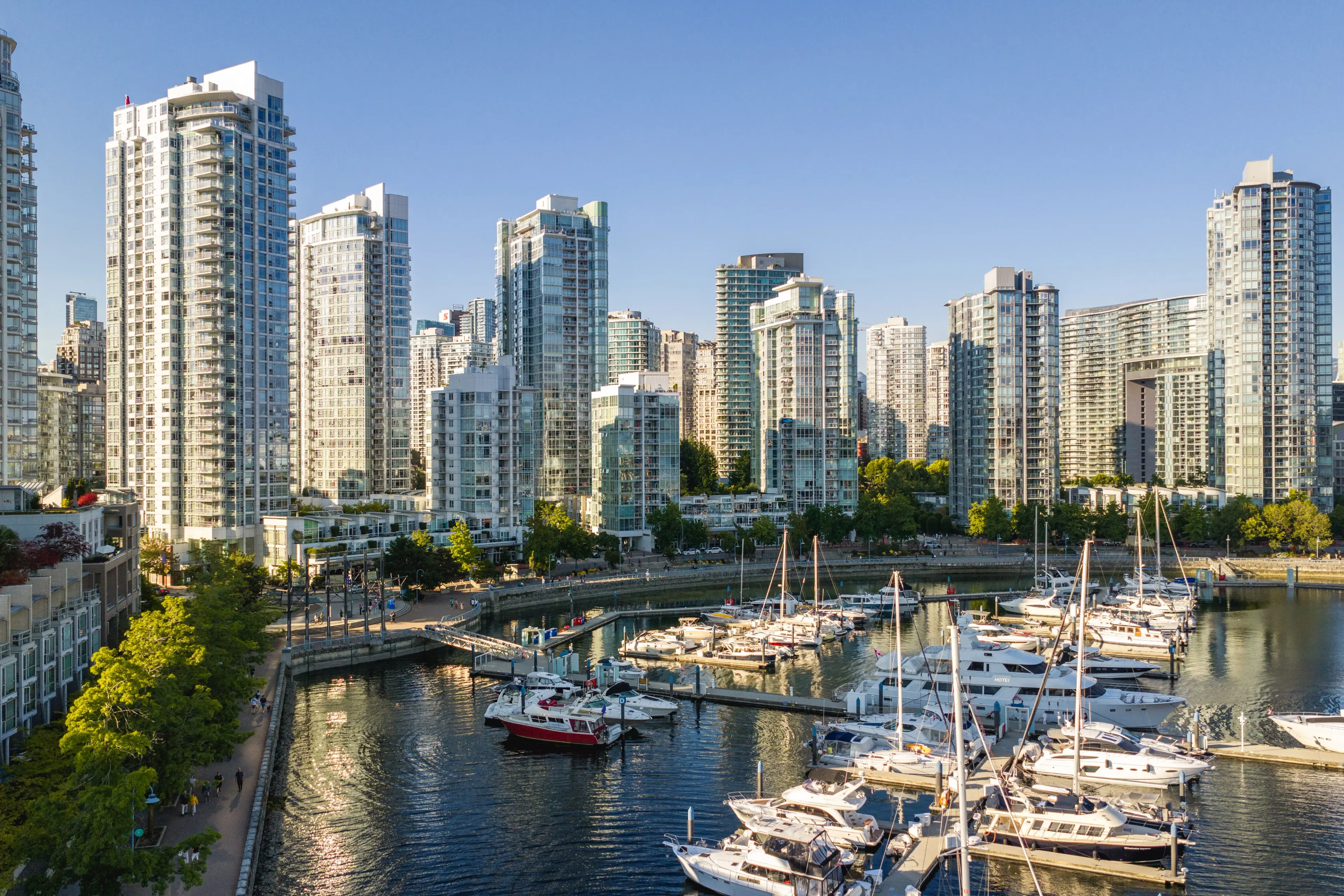 Marina with boats docked and modern high-rise buildings under clear blue sky.