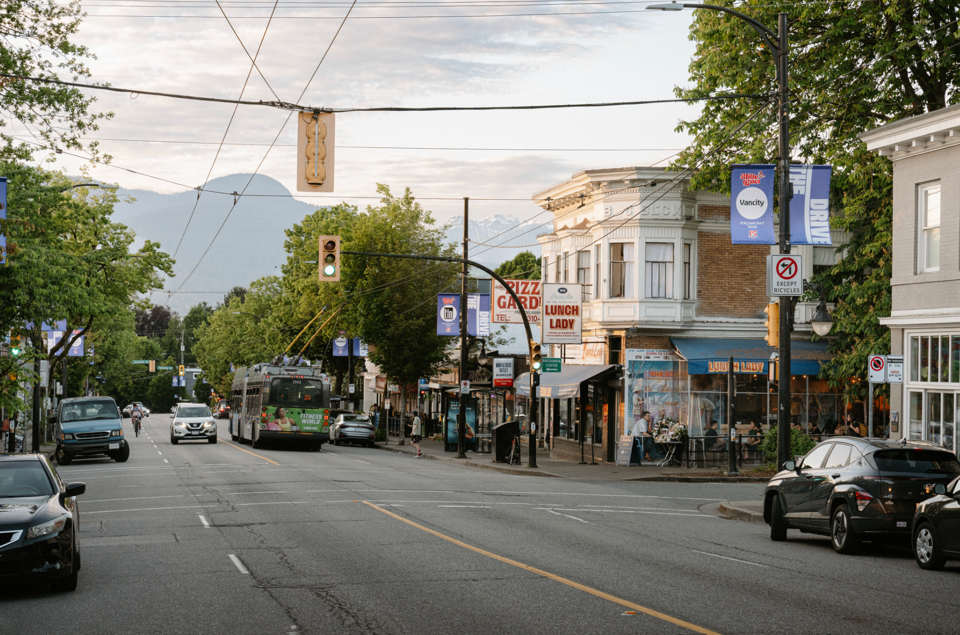Street view with cars, a bus, pedestrians, and buildings including a restaurant named Lunch Lady under a green traffic light.