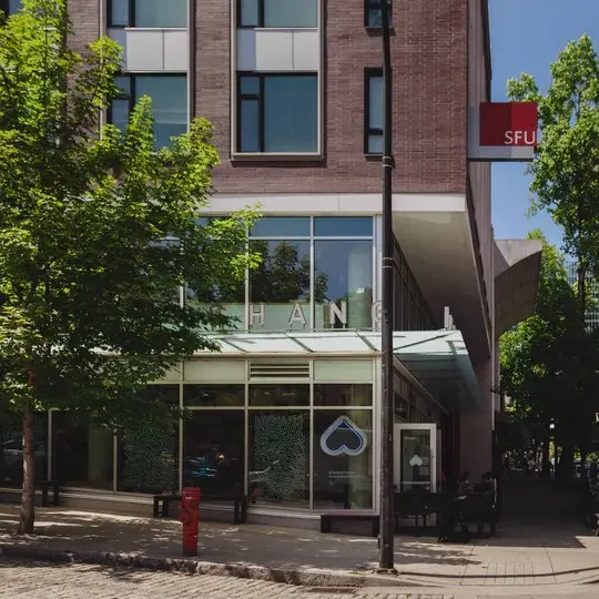 Street view of a building with large windows, trees, a red fire hydrant, and an SFU sign on the corner.