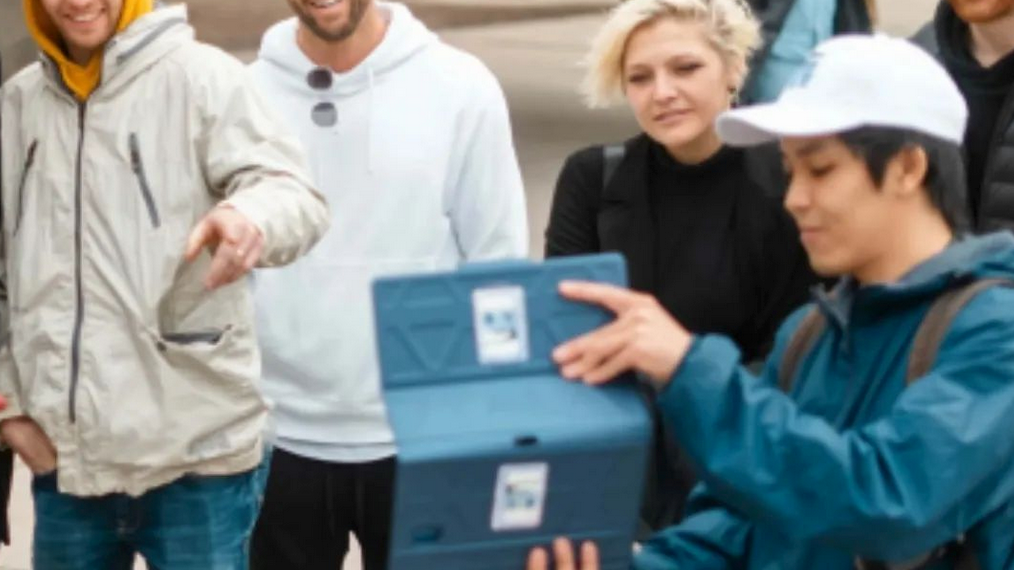 A group watches a clip of a film on an ipad with a tour guide from Vancouver Film and TV Tours