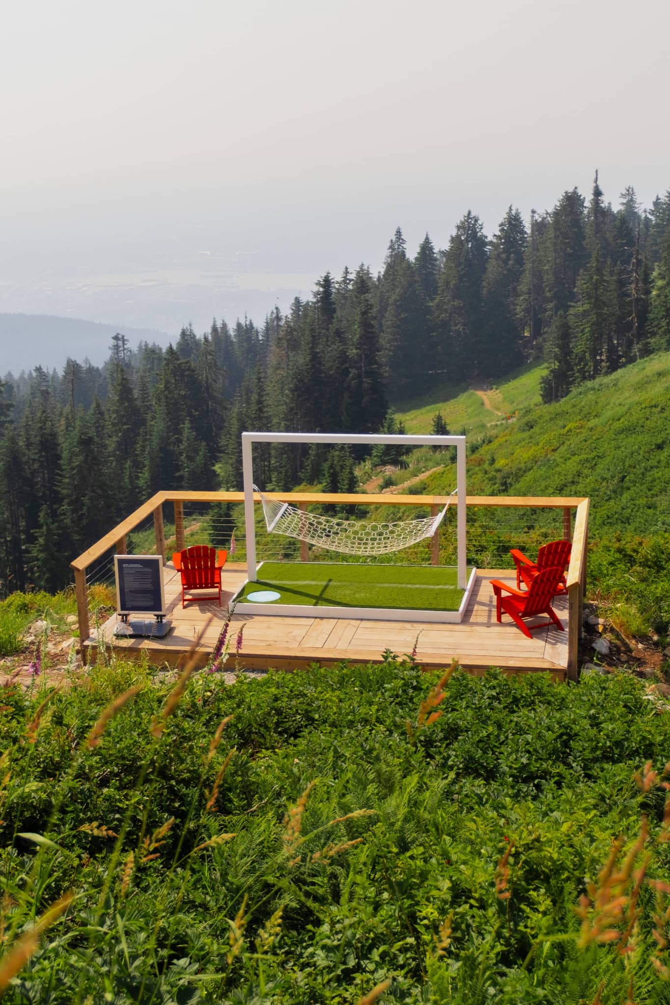 Wooden deck with two red chairs and a white hammock framed by a white structure, overlooking a green forested mountain.