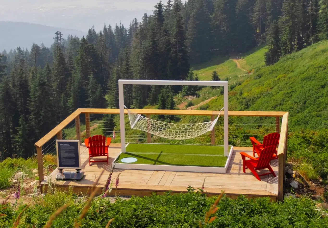 Wooden deck with two red chairs and a white hammock framed by a white structure, overlooking a green forested mountain.