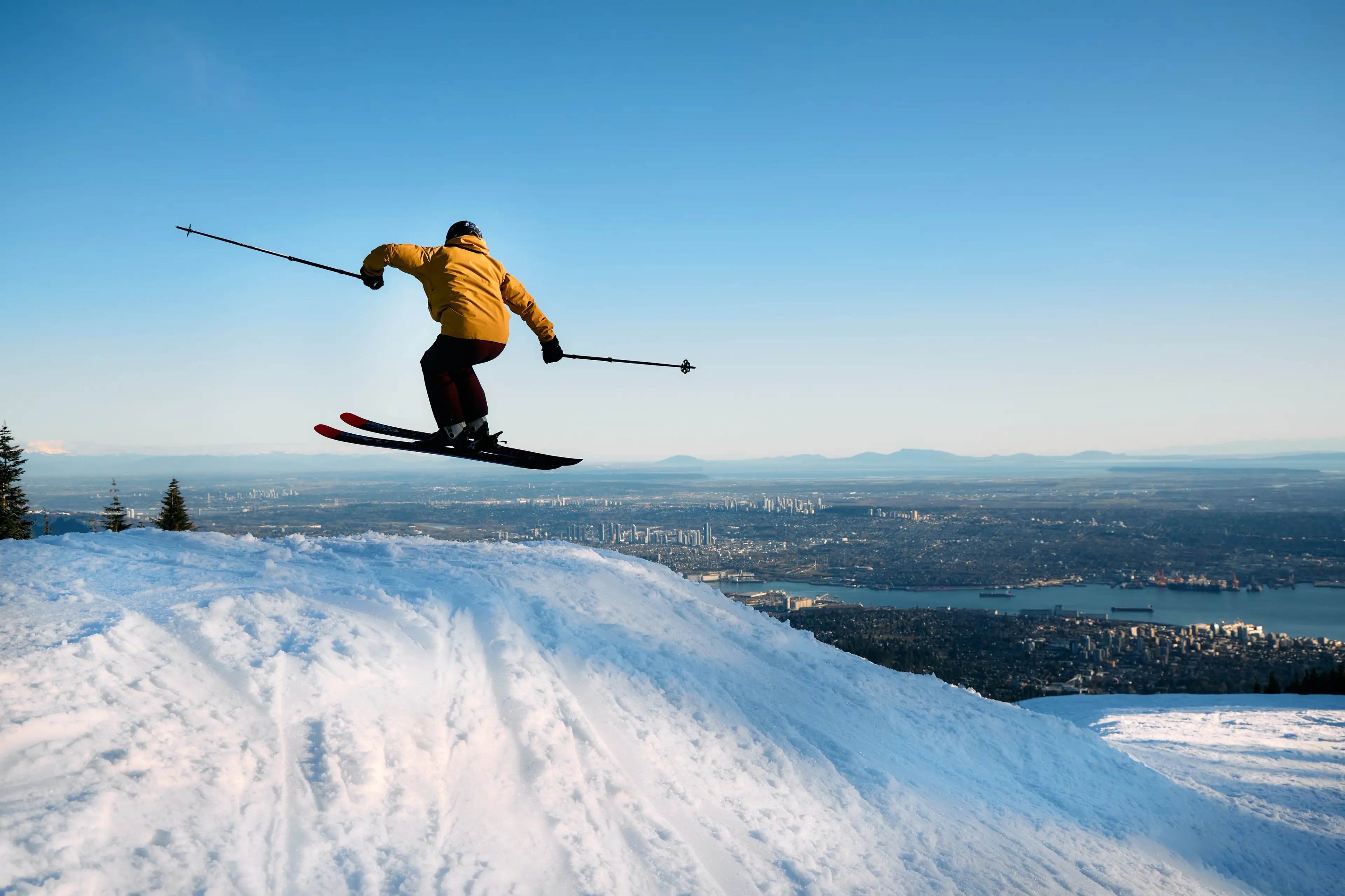 Person jumping on skiies with the vancouver skyline in the background on Cypress Mountain.