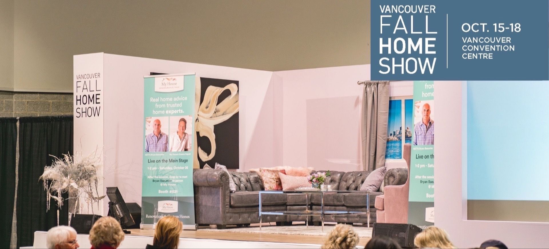 Stage setup with gray sectional sofa, glass coffee table, and banners for Vancouver Fall Home Show at Vancouver Convention Centre.