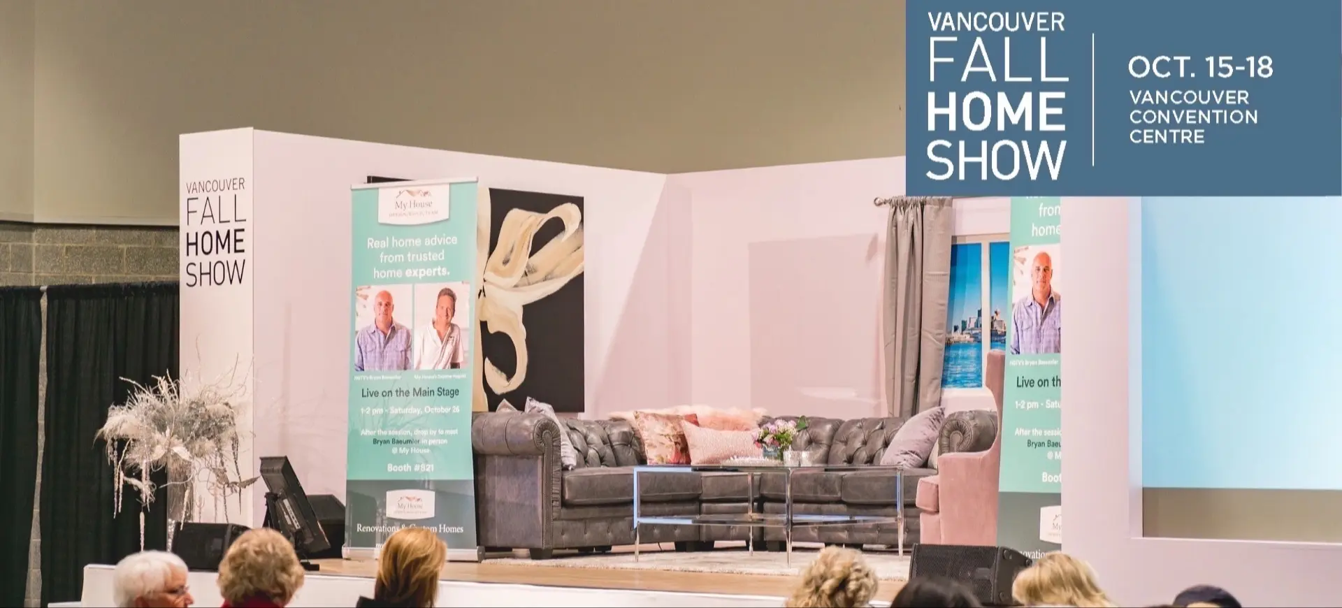 Stage setup with gray sectional sofa, glass coffee table, and banners for Vancouver Fall Home Show at Vancouver Convention Centre.